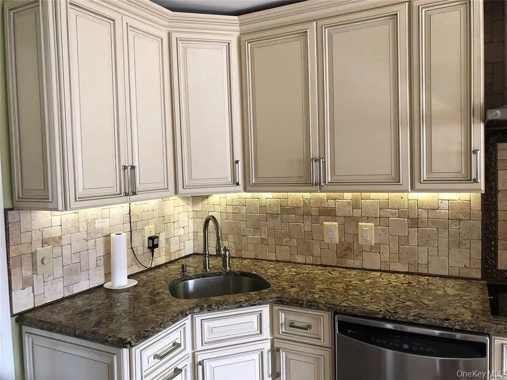 Kitchen featuring dishwasher, dark stone countertops, and tasteful backsplash Kitchen featuring dishwasher, dark stone countertops, and tasteful backsplash