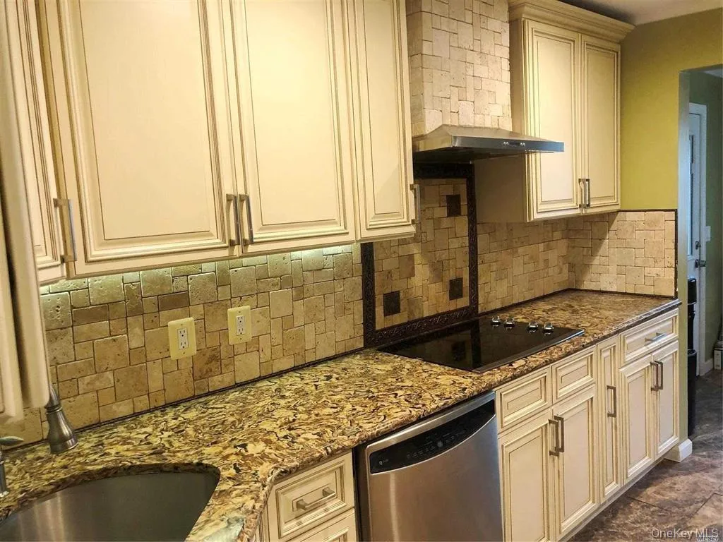 Kitchen featuring dishwasher, cream cabinets, dark stone counters, and black electric stovetop Kitchen featuring dishwasher, cream cabinets, dark stone counters, and black electric stovetop