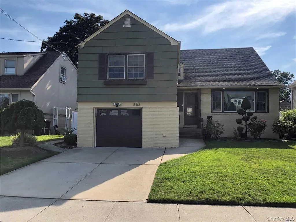Split level home featuring brick siding, a garage, concrete driveway, a front lawn, and a shingled roof Split level home featuring brick siding, a garage, concrete driveway, a front lawn, and a shingled roof