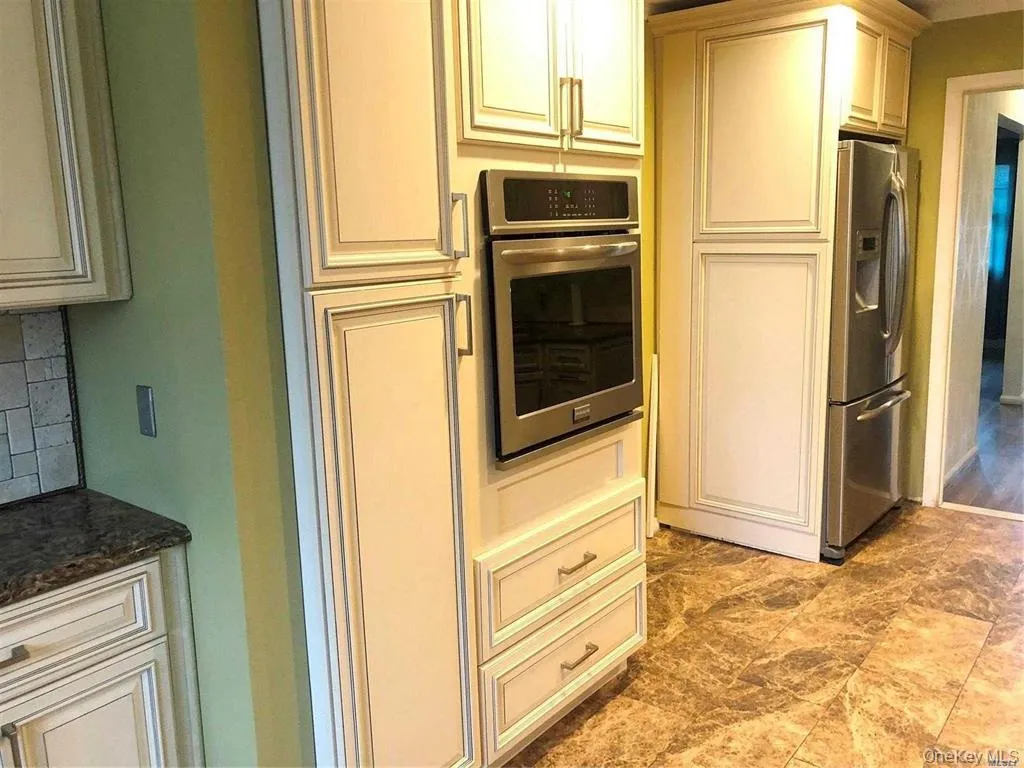 Kitchen featuring appliances with stainless steel finishes, backsplash, dark stone countertops, and cream cabinets Kitchen featuring appliances with stainless steel finishes, backsplash, dark stone countertops, and cream cabinets