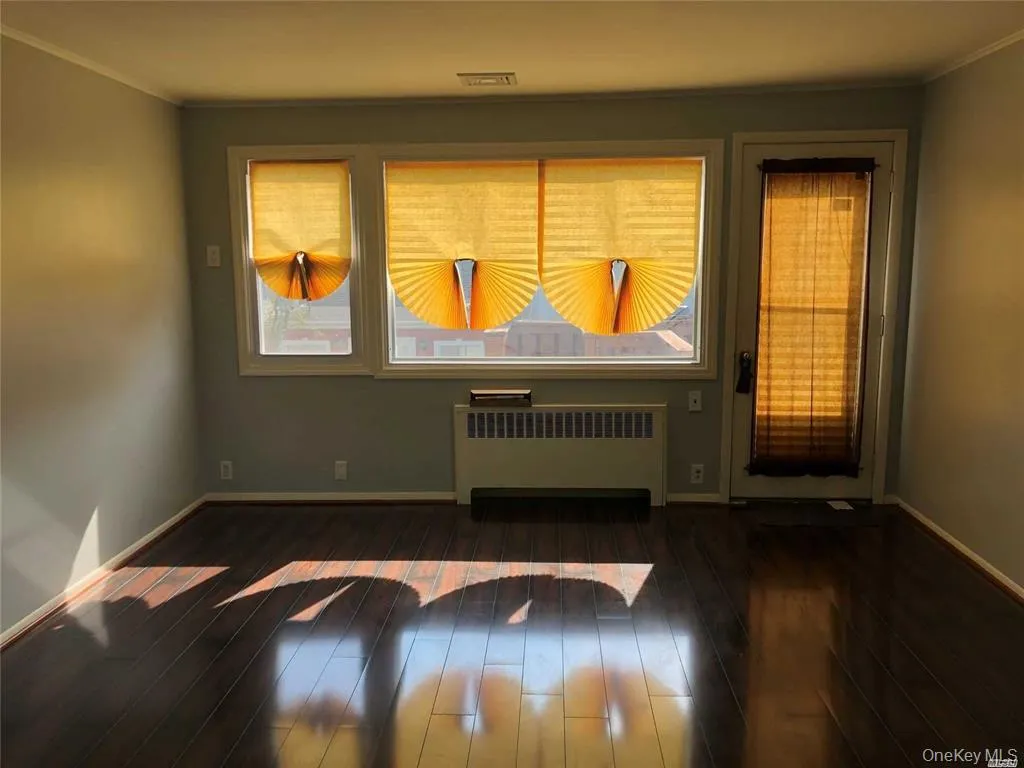 Unfurnished room featuring radiator, ornamental molding, and dark wood-style flooring Unfurnished room featuring radiator, ornamental molding, and dark wood-style flooring
