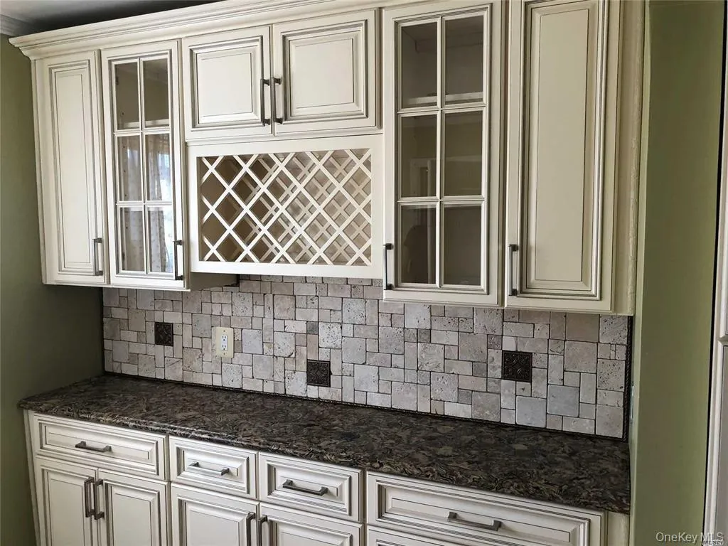 Kitchen featuring decorative backsplash, glass insert cabinets, dark stone countertops, and cream cabinetry Kitchen featuring decorative backsplash, glass insert cabinets, dark stone countertops, and cream cabinetry