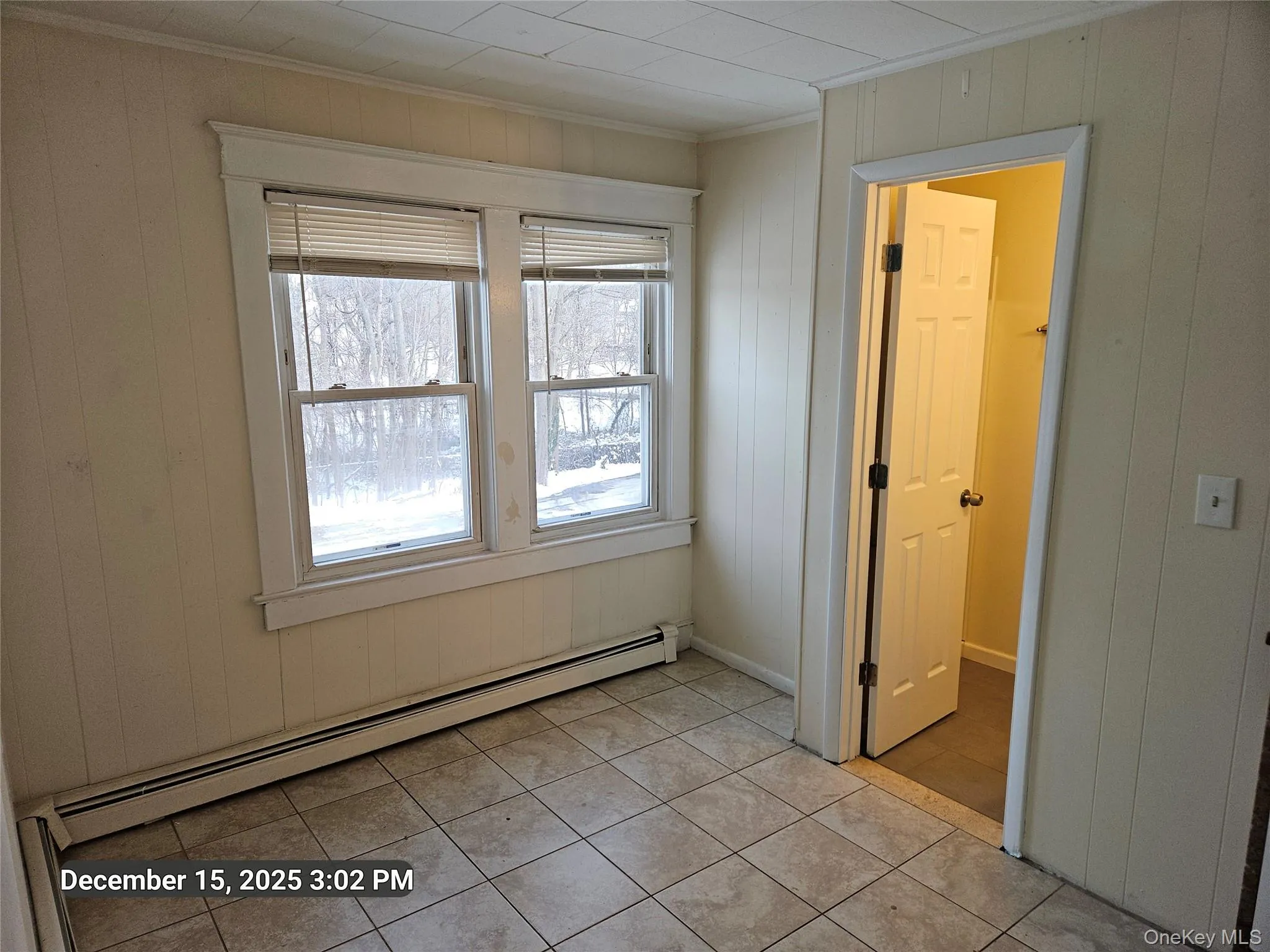 Spare room with baseboard heating, light tile patterned floors, and wood walls Spare room with baseboard heating, light tile patterned floors, and wood walls