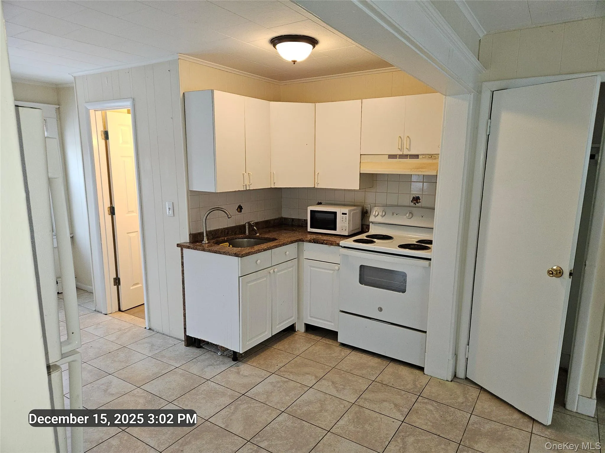 Kitchen featuring white appliances, crown molding, white cabinets, under cabinet range hood, and backsplash Kitchen featuring white appliances, crown molding, white cabinets, under cabinet range hood, and backsplash