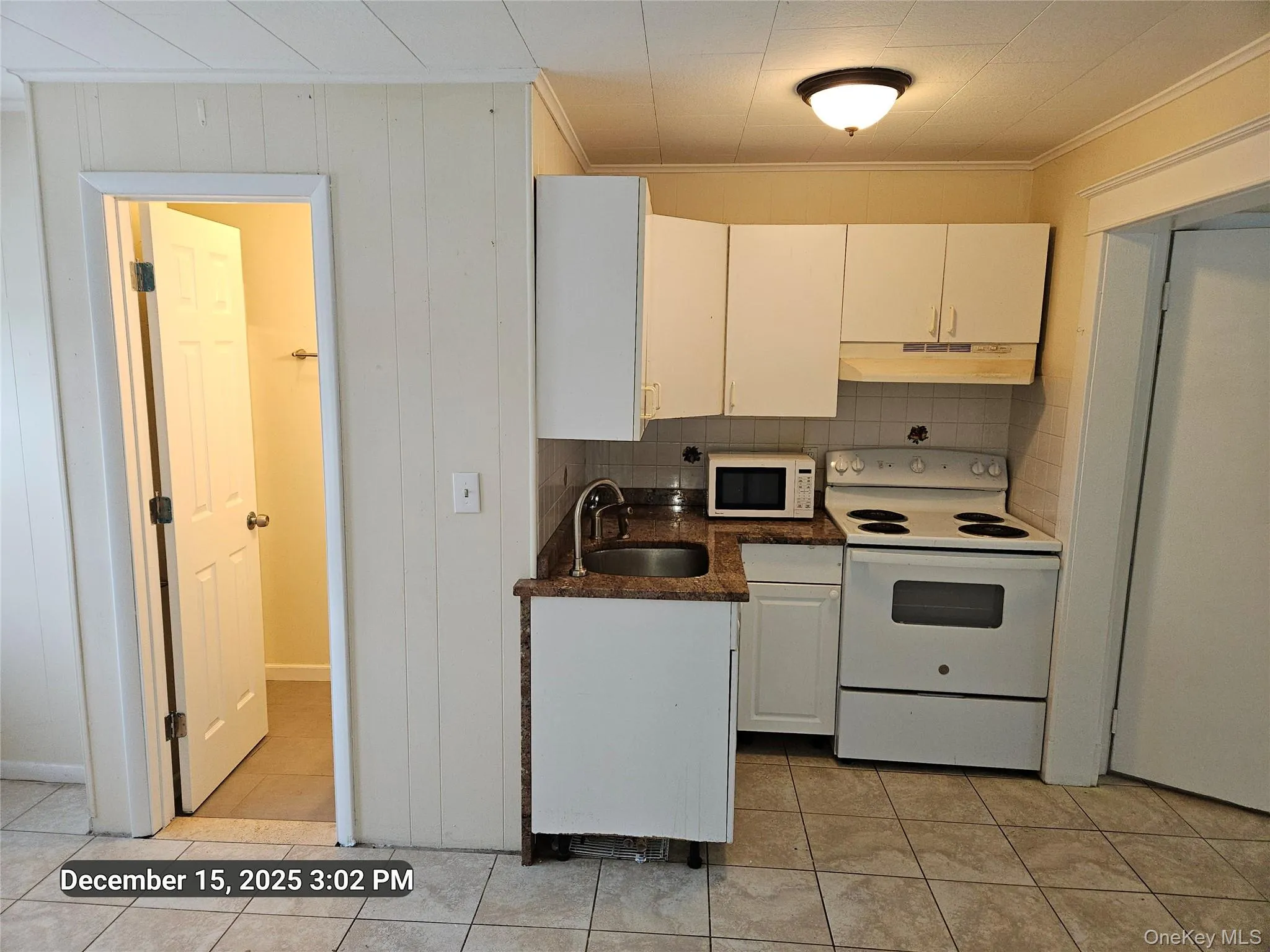 Kitchen featuring white appliances, white cabinets, decorative backsplash, under cabinet range hood, and ornamental molding Kitchen featuring white appliances, white cabinets, decorative backsplash, under cabinet range hood, and ornamental molding