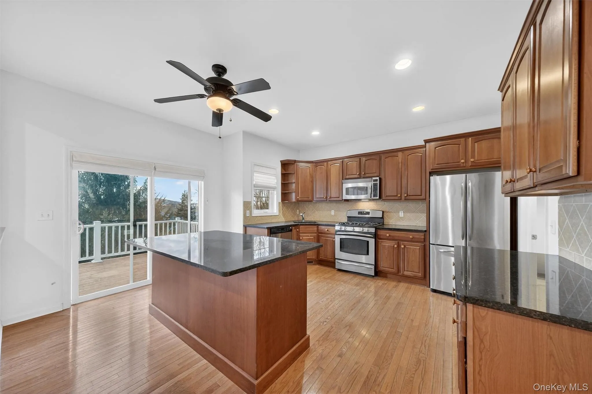 Kitchen with open shelves, dark stone countertops, brown cabinetry, appliances with stainless steel finishes, and backsplash Kitchen with open shelves, dark stone countertops, brown cabinetry, appliances with stainless steel finishes, and backsplash