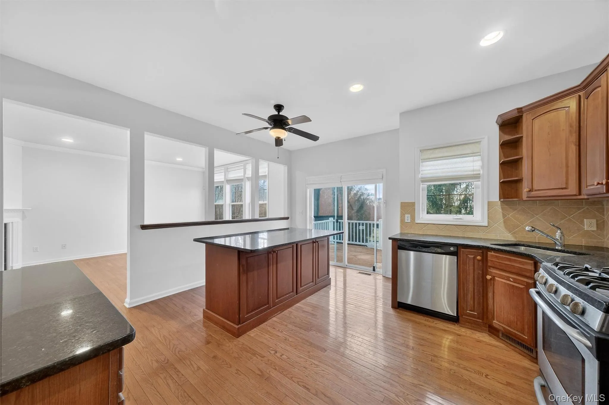 Kitchen featuring appliances with stainless steel finishes, brown cabinetry, dark stone counters, light wood-type flooring, and recessed lighting Kitchen featuring appliances with stainless steel finishes, brown cabinetry, dark stone counters, light wood-type flooring, and recessed lighting