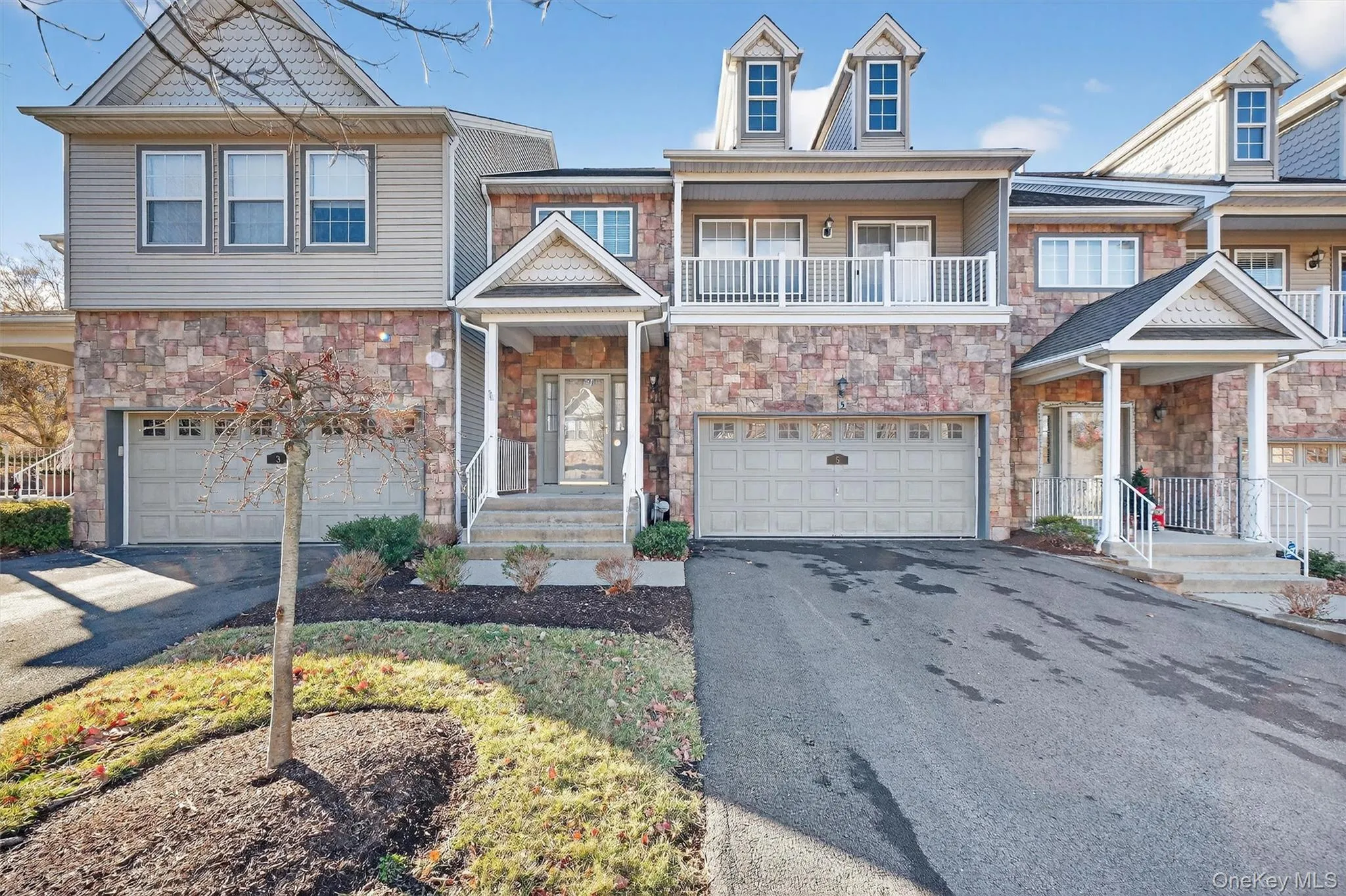 View of front facade featuring asphalt driveway, a balcony, stone siding, and an attached garage View of front facade featuring asphalt driveway, a balcony, stone siding, and an attached garage