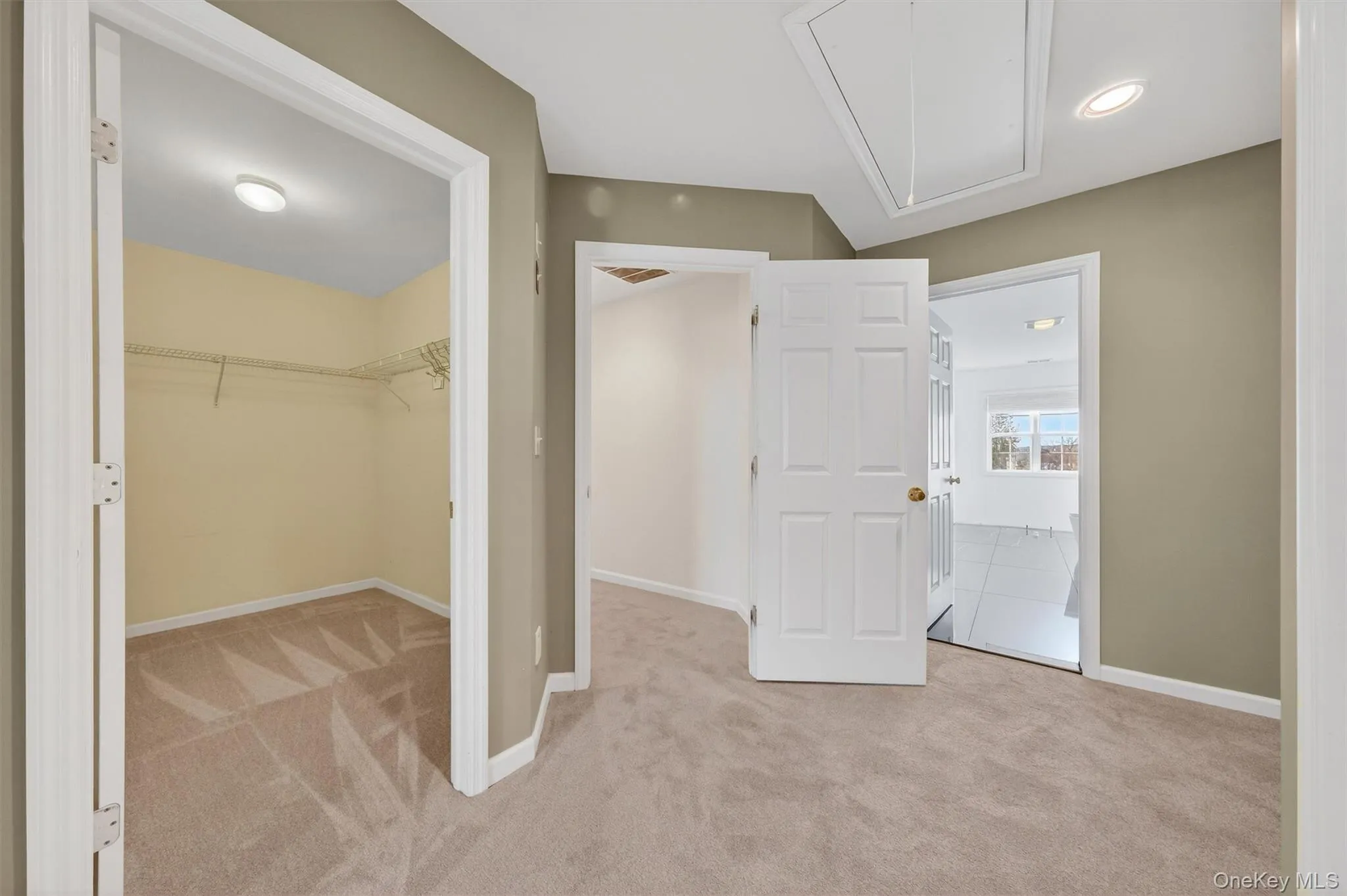 Unfurnished bedroom featuring attic access, light colored carpet, and a walk in closet Unfurnished bedroom featuring attic access, light colored carpet, and a walk in closet
