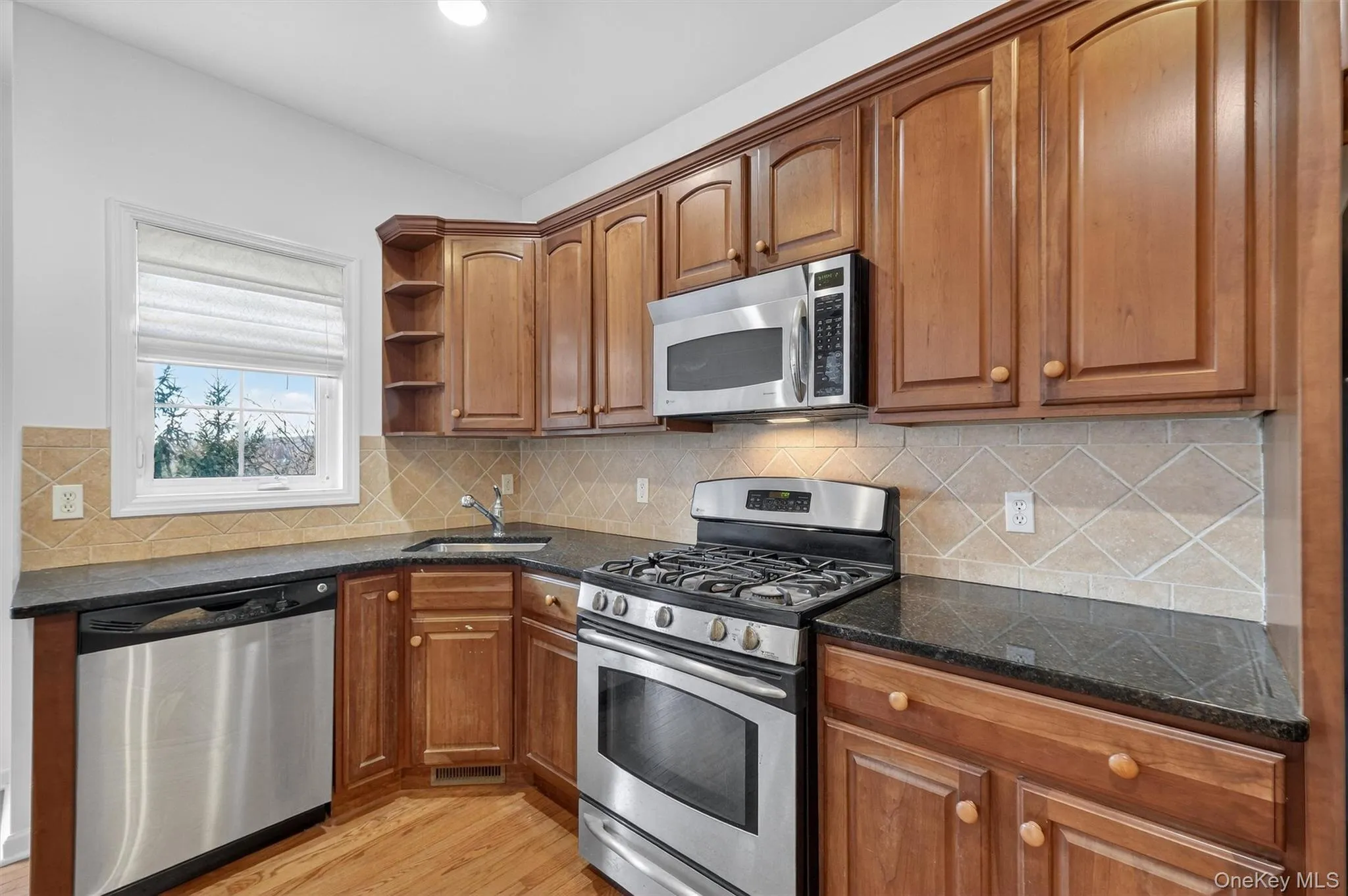 Kitchen featuring appliances with stainless steel finishes, light wood finished floors, open shelves, and dark stone counters Kitchen featuring appliances with stainless steel finishes, light wood finished floors, open shelves, and dark stone counters