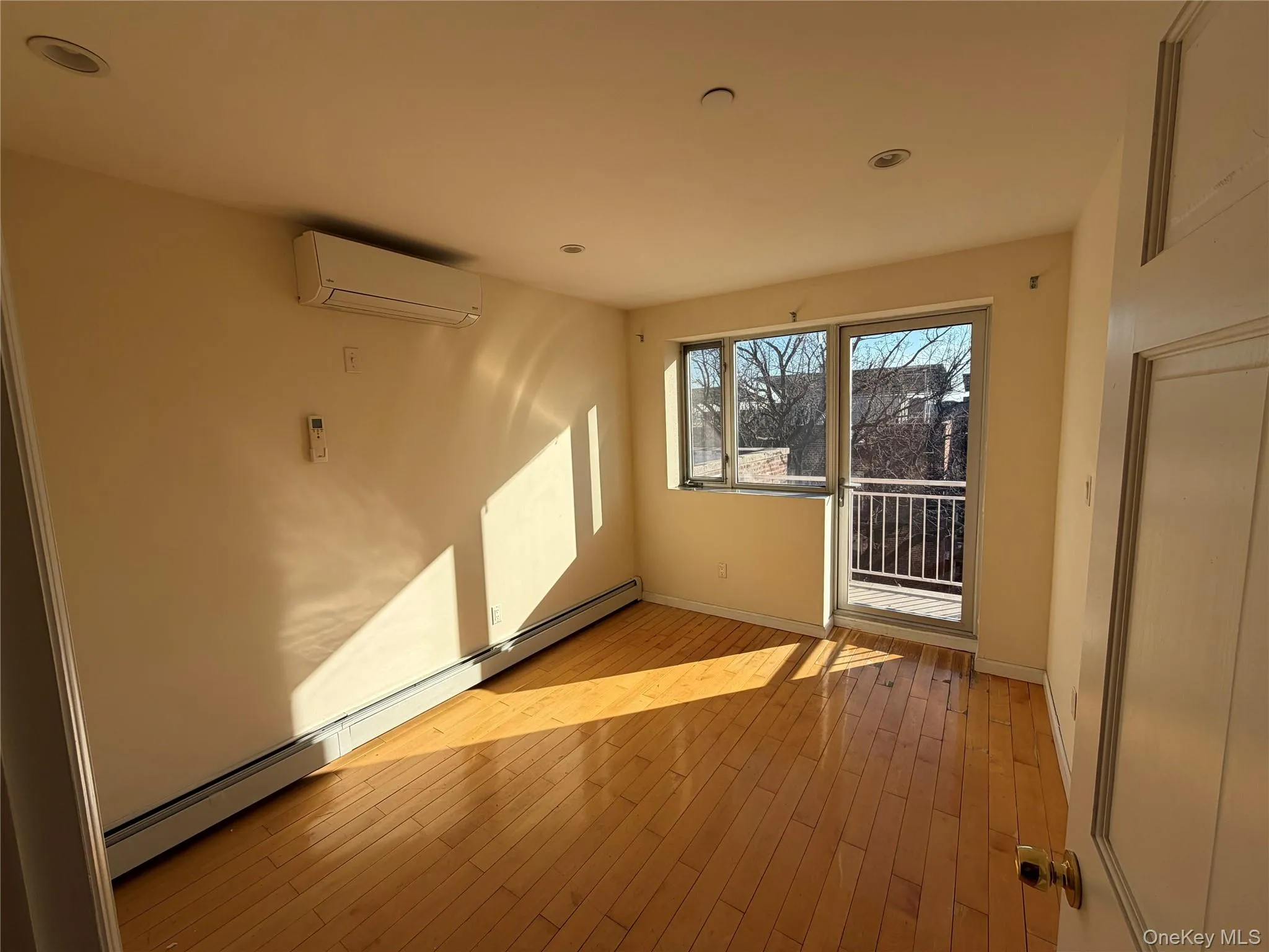 Unfurnished room with baseboard heating, light wood-style floors, a wall unit AC, and recessed lighting Unfurnished room with baseboard heating, light wood-style floors, a wall unit AC, and recessed lighting