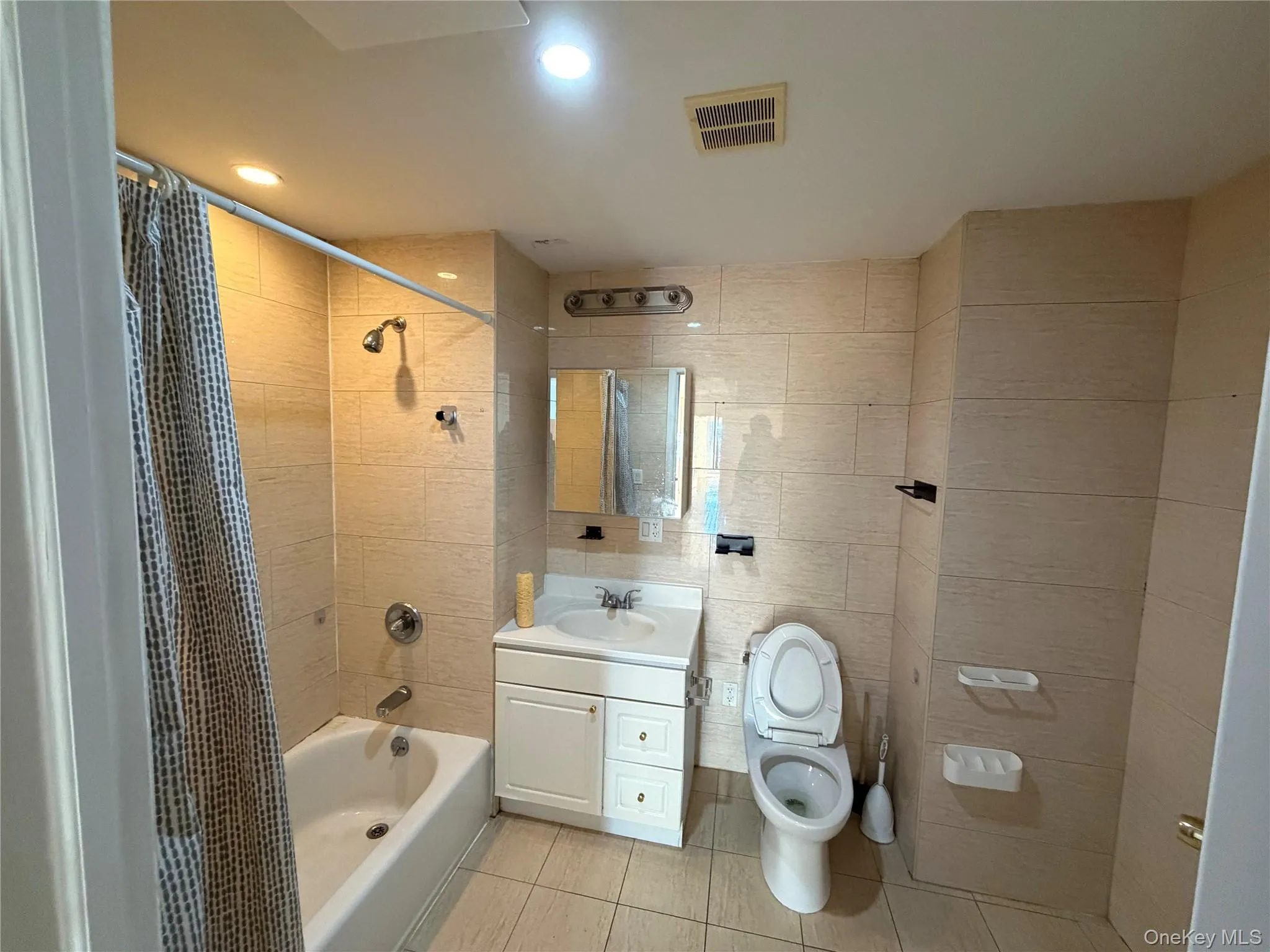 Bathroom featuring vanity, tile walls, shower / bath combination with curtain, light tile patterned floors, and recessed lighting Bathroom featuring vanity, tile walls, shower / bath combination with curtain, light tile patterned floors, and recessed lighting