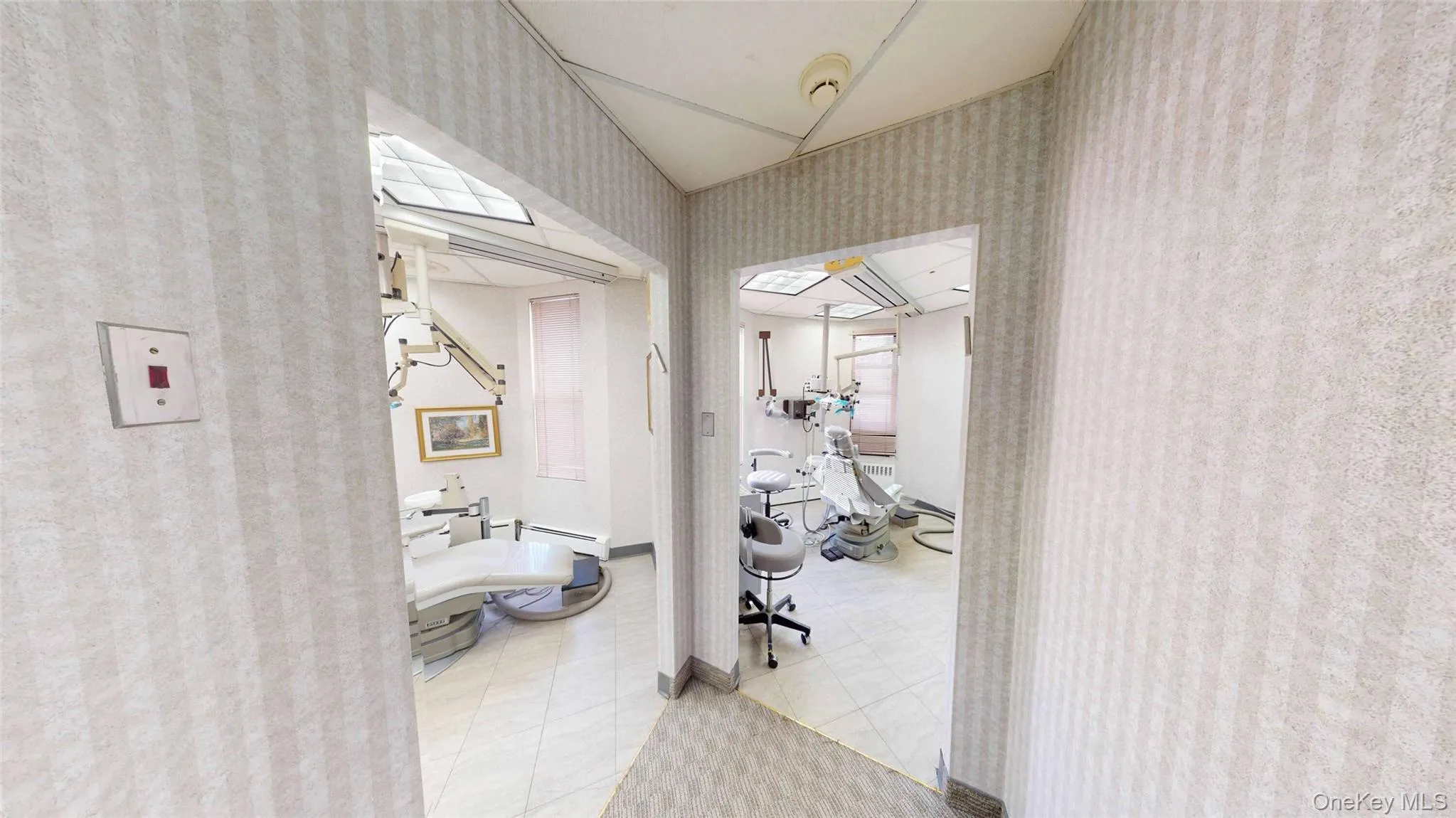 Hallway with wallpapered walls and light tile patterned floors and dental chairs Hallway with wallpapered walls and light tile patterned floors and dental chairs