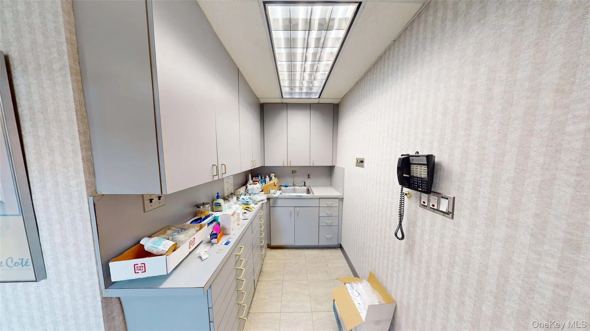Kitchen or Lab with sink featuring light countertops, gray cabinetry, light tile patterned flooring, and wallpapered walls Kitchen or Lab with sink featuring light countertops, gray cabinetry, light tile patterned flooring, and wallpapered walls