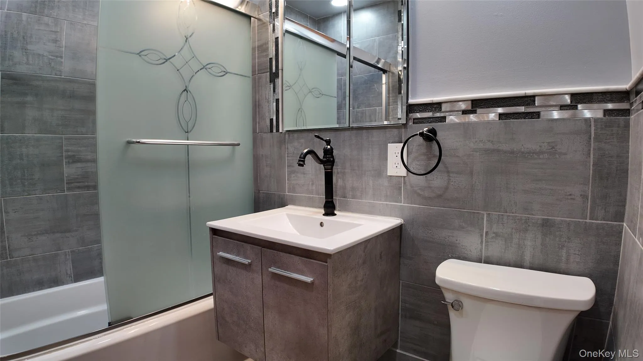 Full bath featuring vanity, tile walls, and bath / shower combo with glass door Full bath featuring vanity, tile walls, and bath / shower combo with glass door