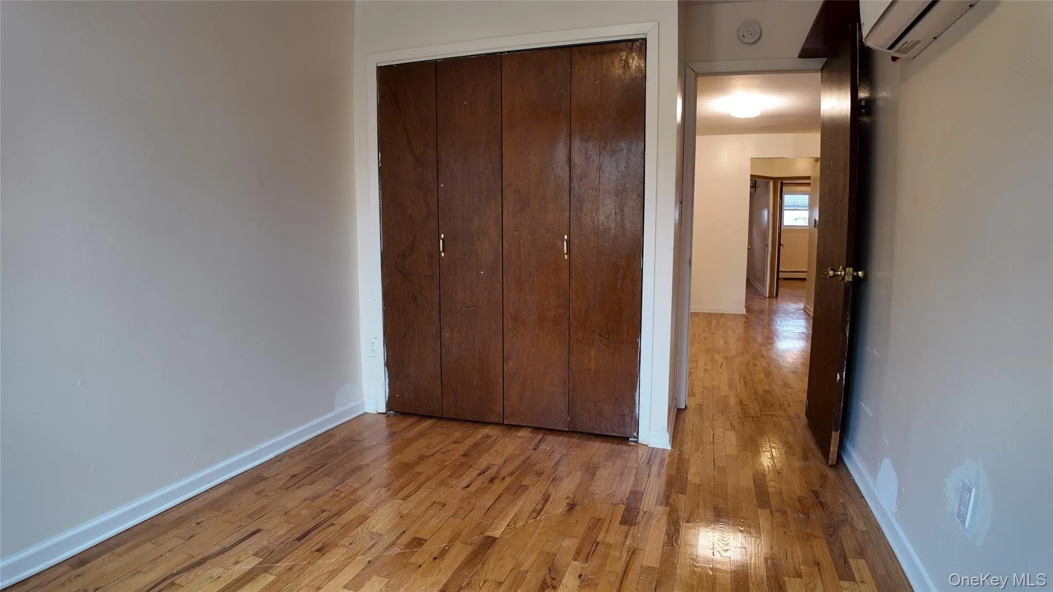 Unfurnished bedroom featuring hardwood / wood-style floors, a wall mounted air conditioner, and a closet Unfurnished bedroom featuring hardwood / wood-style floors, a wall mounted air conditioner, and a closet