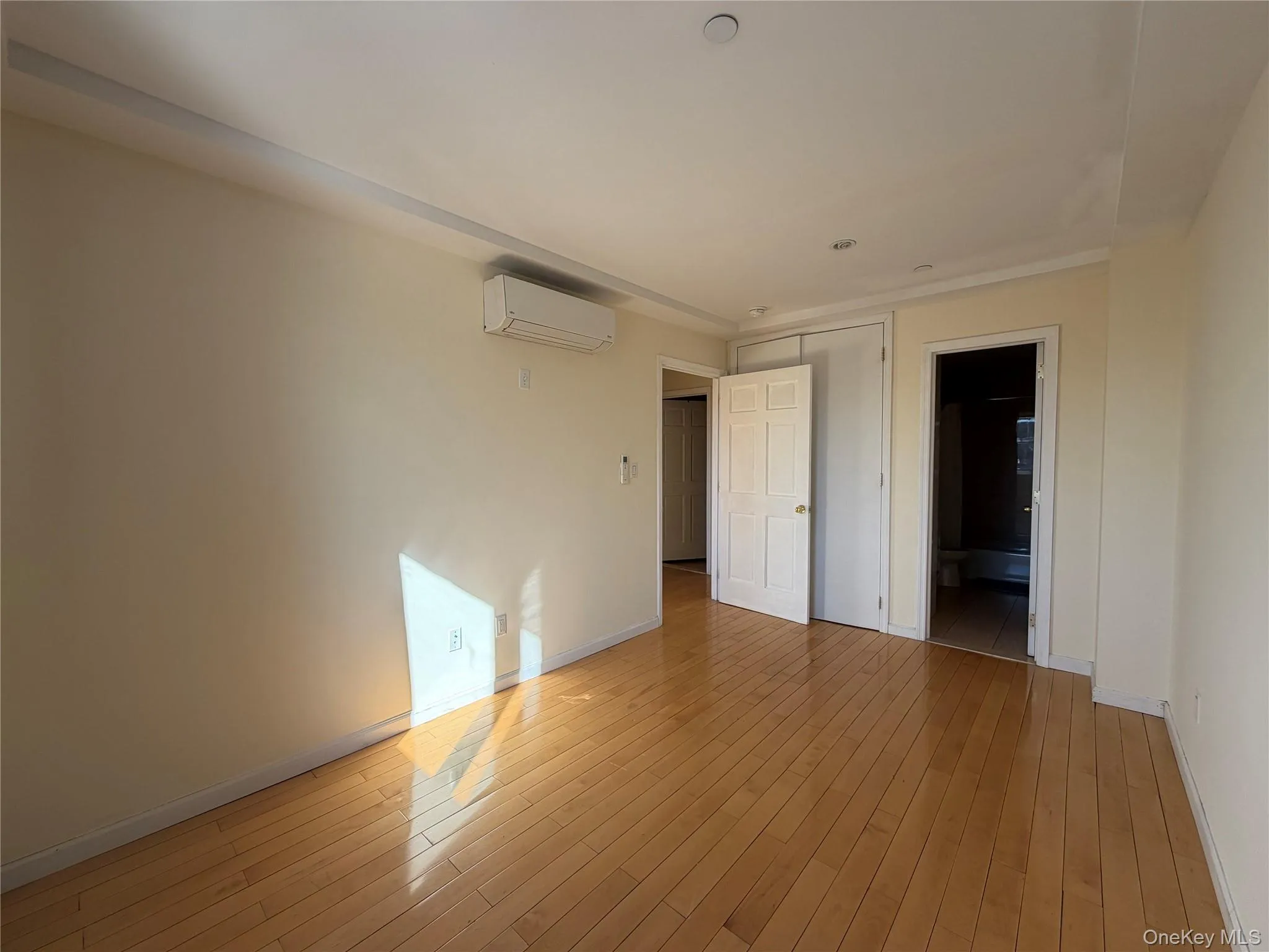 Unfurnished bedroom featuring light wood-type flooring, ensuite bath, and a wall mounted mini split Unfurnished bedroom featuring light wood-type flooring, ensuite bath, and a wall mounted mini split