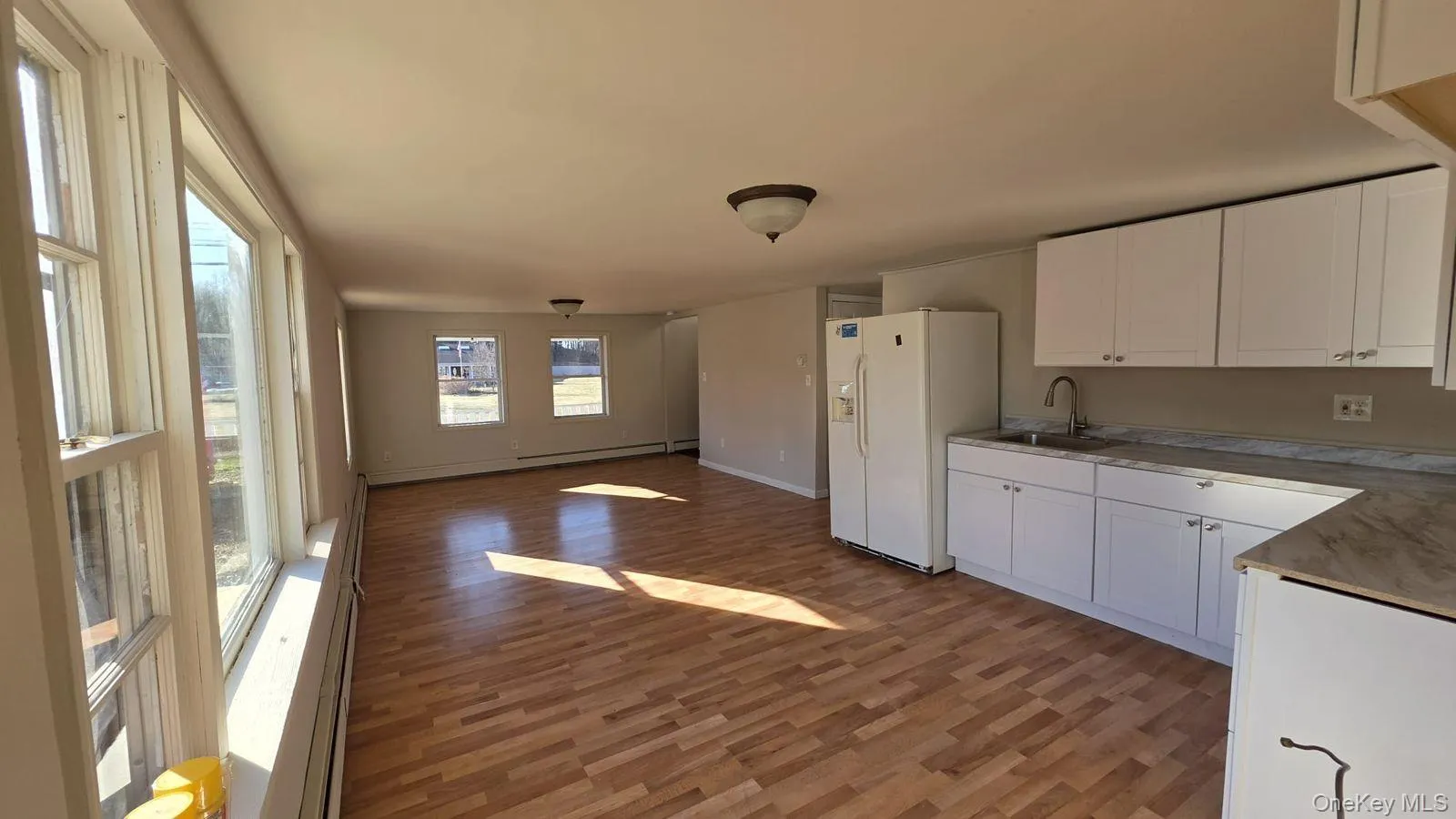 Kitchen with white cabinets, light wood-style floors, white refrigerator with ice dispenser, open floor plan, and a baseboard radiator Kitchen with white cabinets, light wood-style floors, white refrigerator with ice dispenser, open floor plan, and a baseboard radiator