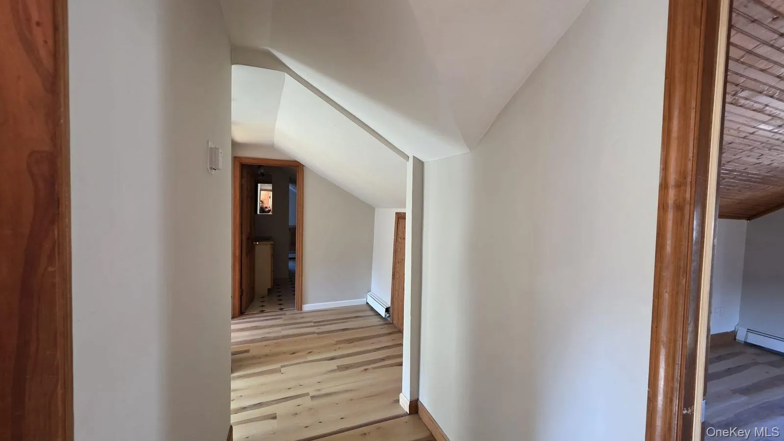 Hall with light wood finished floors, lofted ceiling, and a baseboard heating unit Hall with light wood finished floors, lofted ceiling, and a baseboard heating unit