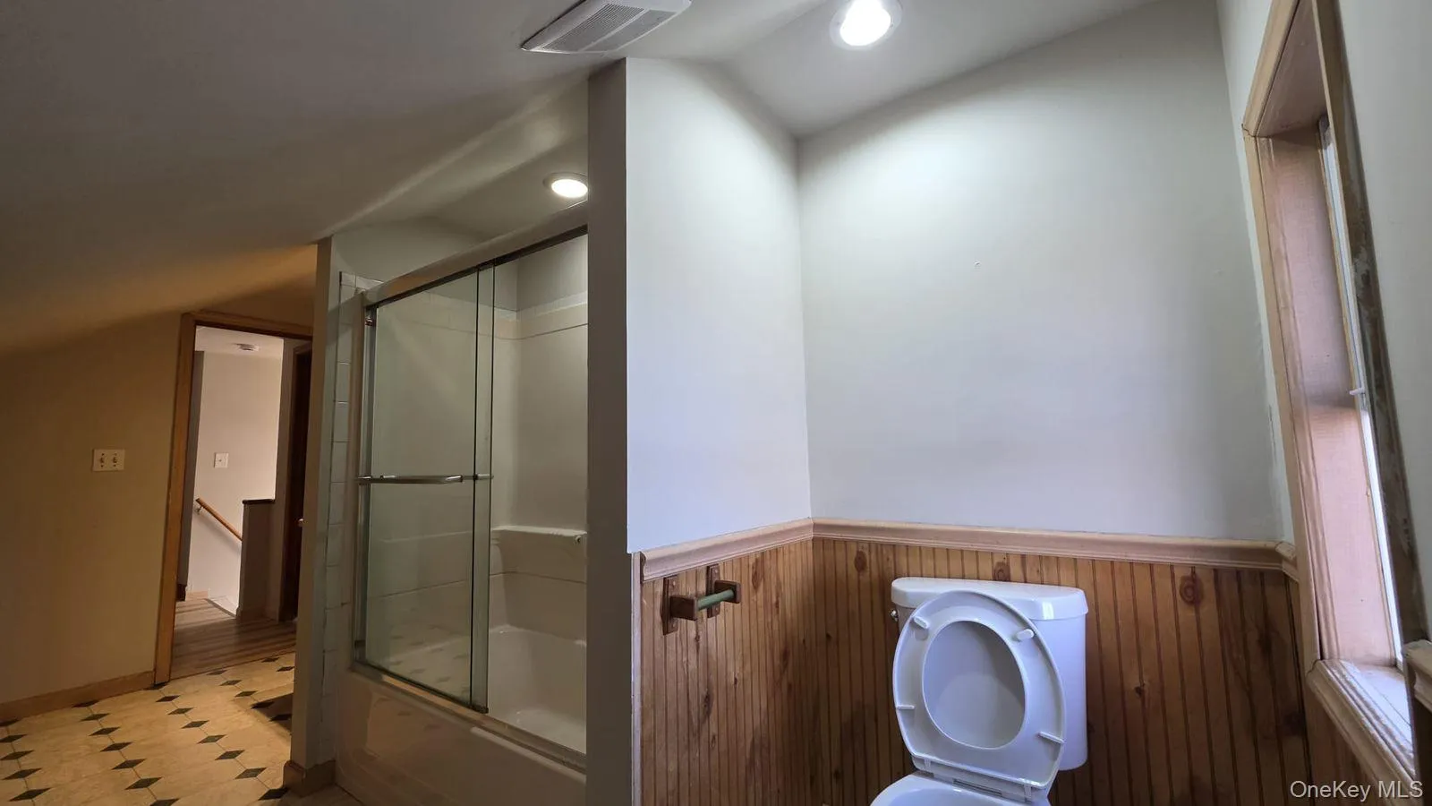 Full bath with bath / shower combo with glass door, wainscoting, and wood walls Full bath with bath / shower combo with glass door, wainscoting, and wood walls