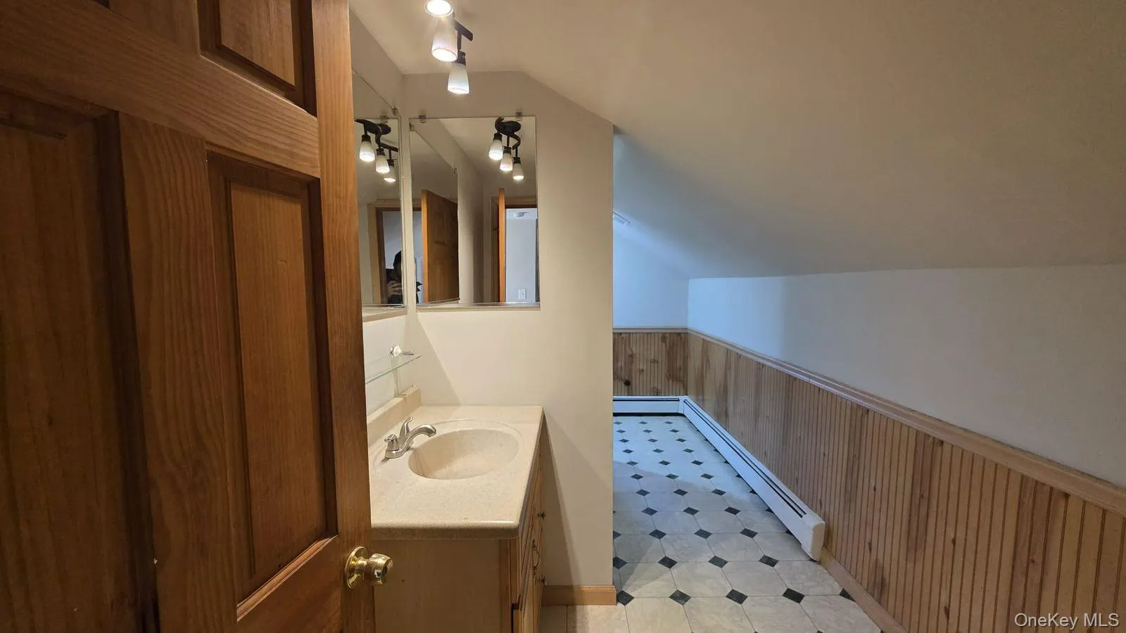 Bathroom with wood walls, wainscoting, vaulted ceiling, vanity, and a baseboard radiator Bathroom with wood walls, wainscoting, vaulted ceiling, vanity, and a baseboard radiator
