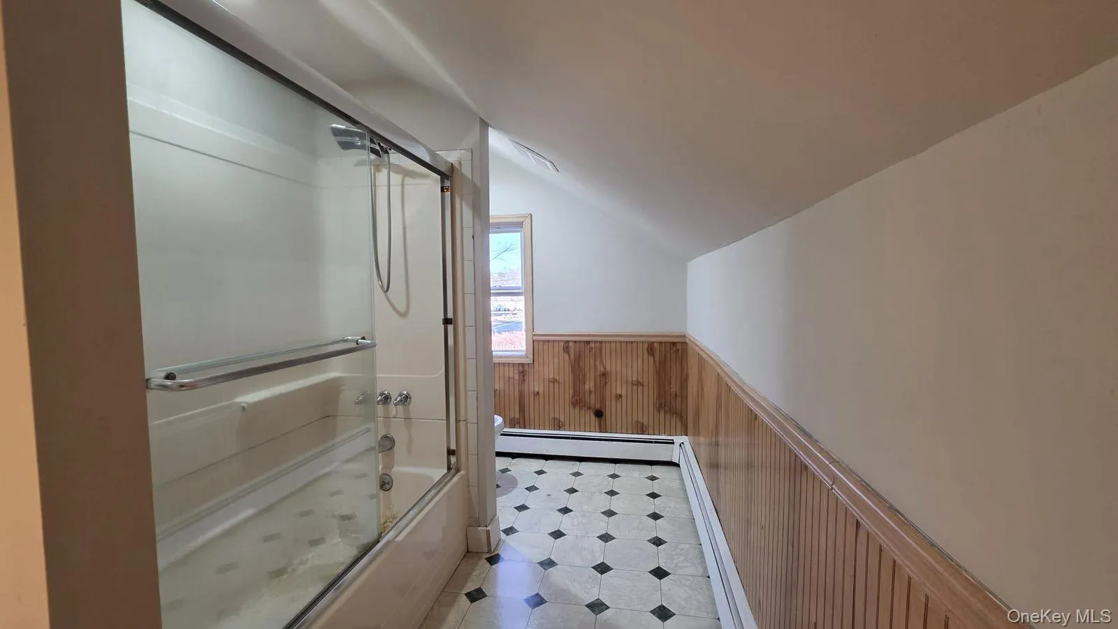 Full bath with a wainscoted wall, wooden walls, bath / shower combo with glass door, vaulted ceiling, and a baseboard heating unit Full bath with a wainscoted wall, wooden walls, bath / shower combo with glass door, vaulted ceiling, and a baseboard heating unit