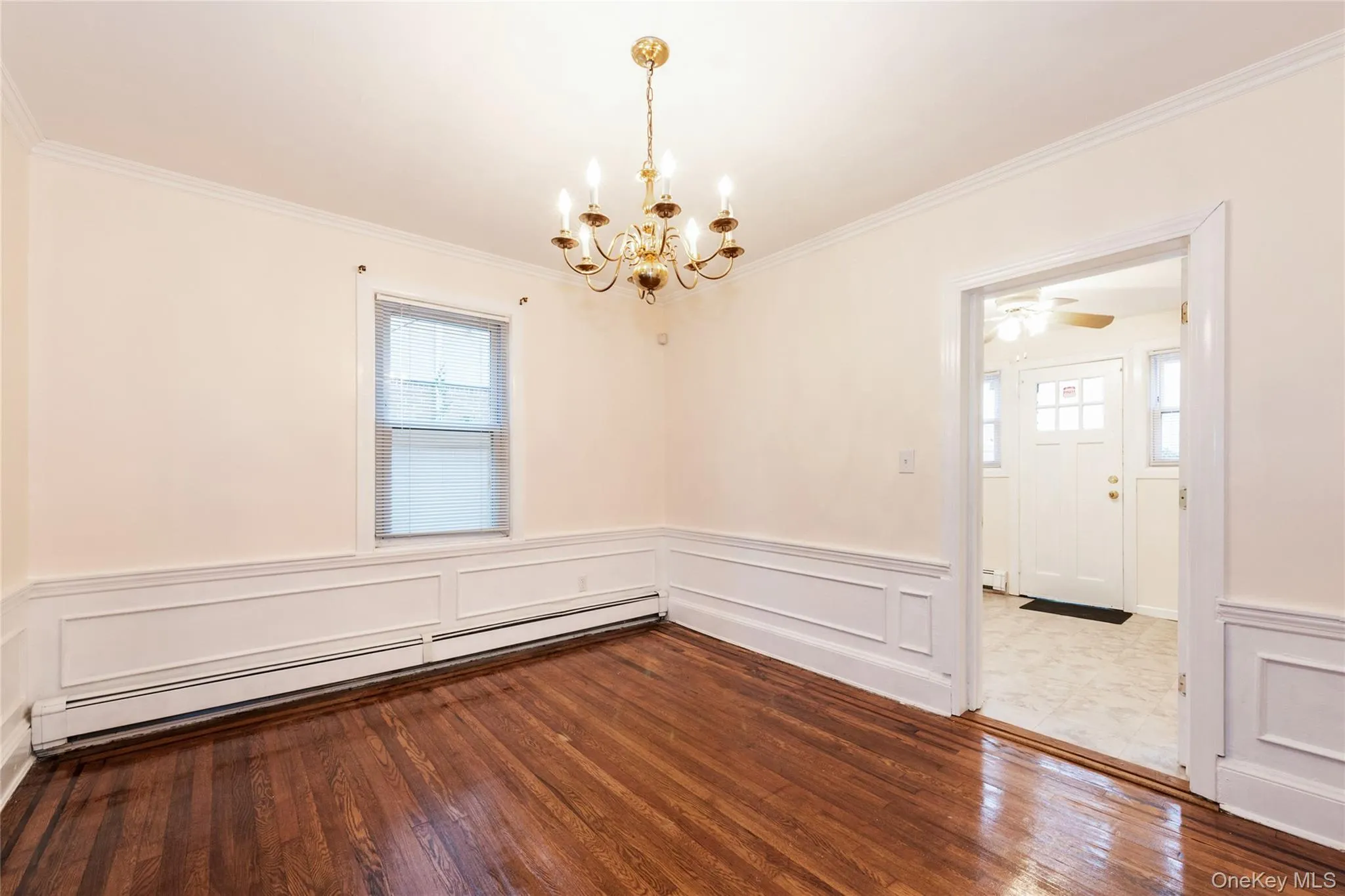 Dining room with hardwood flooring, a baseboard radiator, a chandelier, crown molding, and a wainscoted wall. Dining room with hardwood flooring, a baseboard radiator, a chandelier, crown molding, and a wainscoted wall.