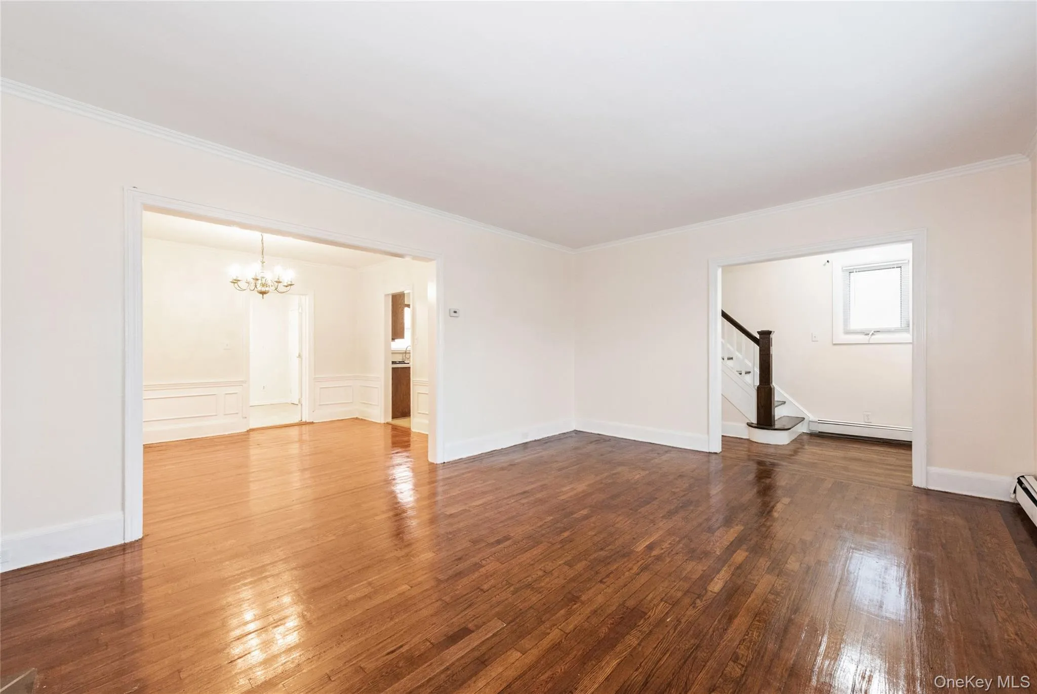 Unfurnished living room featuring hardwood flooring, and crown molding. Unfurnished living room featuring hardwood flooring, and crown molding.