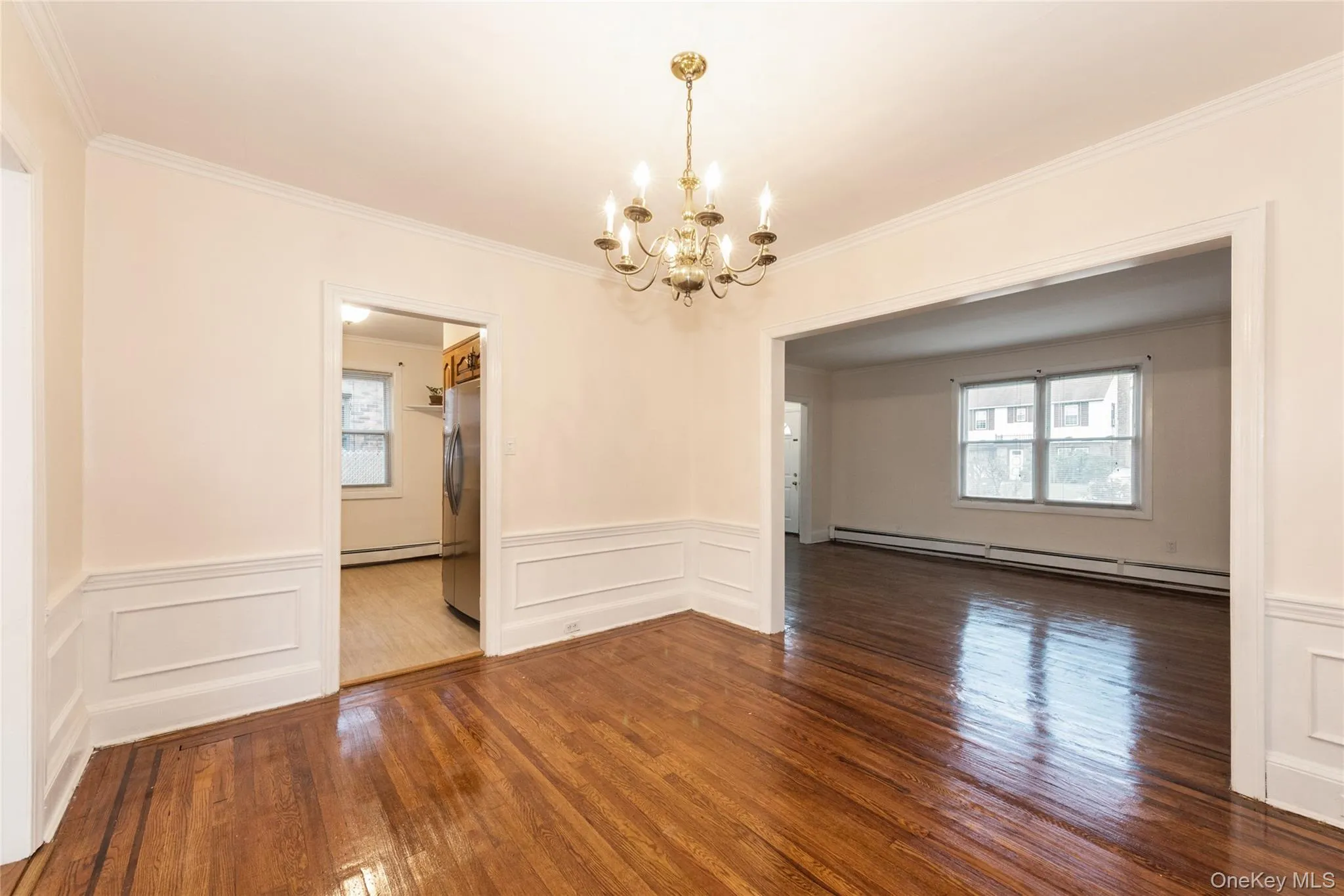 Dining room with hardwood flooring, a baseboard radiator, a chandelier, crown molding, and a wainscoted wall. Dining room with hardwood flooring, a baseboard radiator, a chandelier, crown molding, and a wainscoted wall.