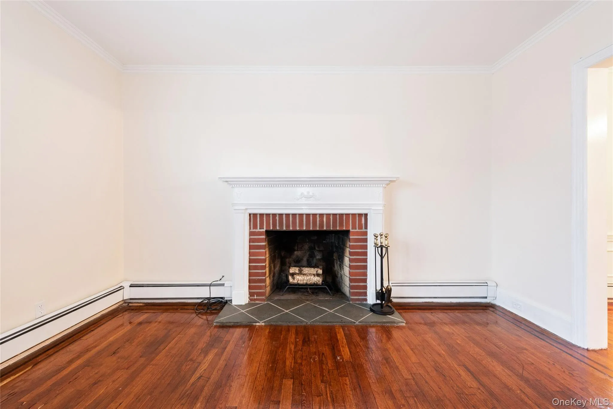 Detailed view of a tile fireplace, ornamental molding, baseboard heating, and hardwood finished floors. Detailed view of a tile fireplace, ornamental molding, baseboard heating, and hardwood finished floors.