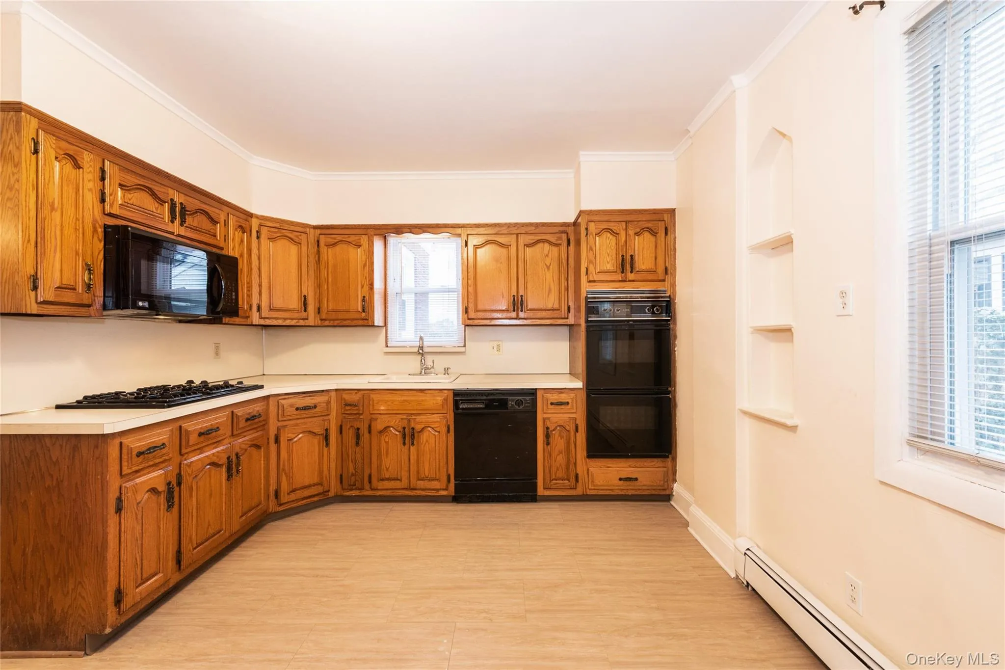 Eat-In-Kitchen with brown cabinets, light countertops, a baseboard radiator, black appliances, and crown molding. Eat-In-Kitchen with brown cabinets, light countertops, a baseboard radiator, black appliances, and crown molding.