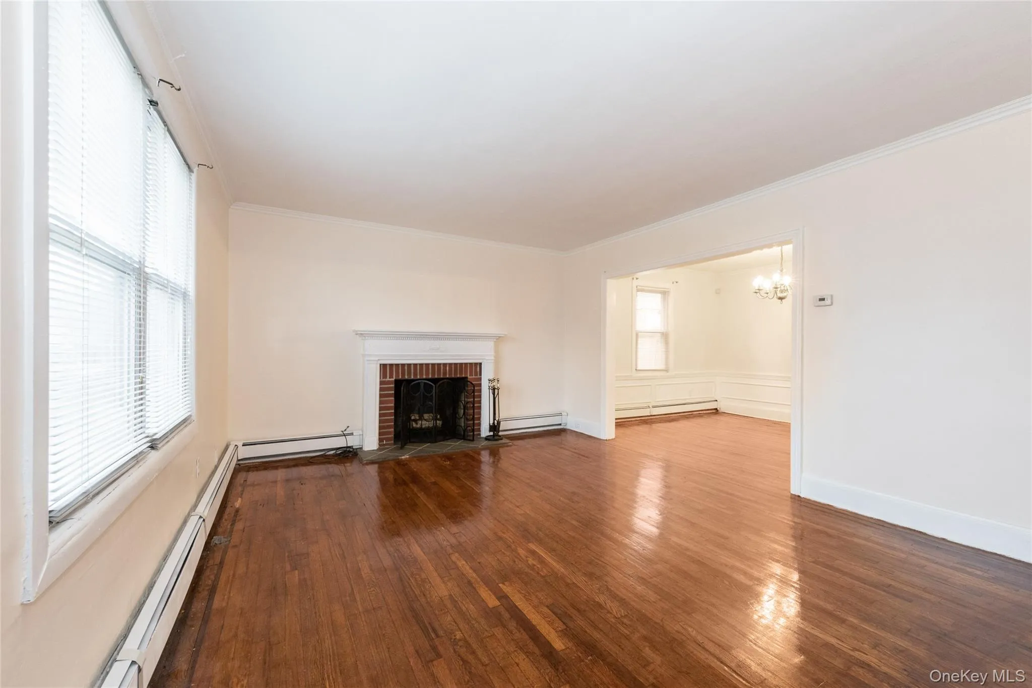 Unfurnished living room with baseboard heating, a fireplace, hardwood flooring, and ornamental molding. Unfurnished living room with baseboard heating, a fireplace, hardwood flooring, and ornamental molding.