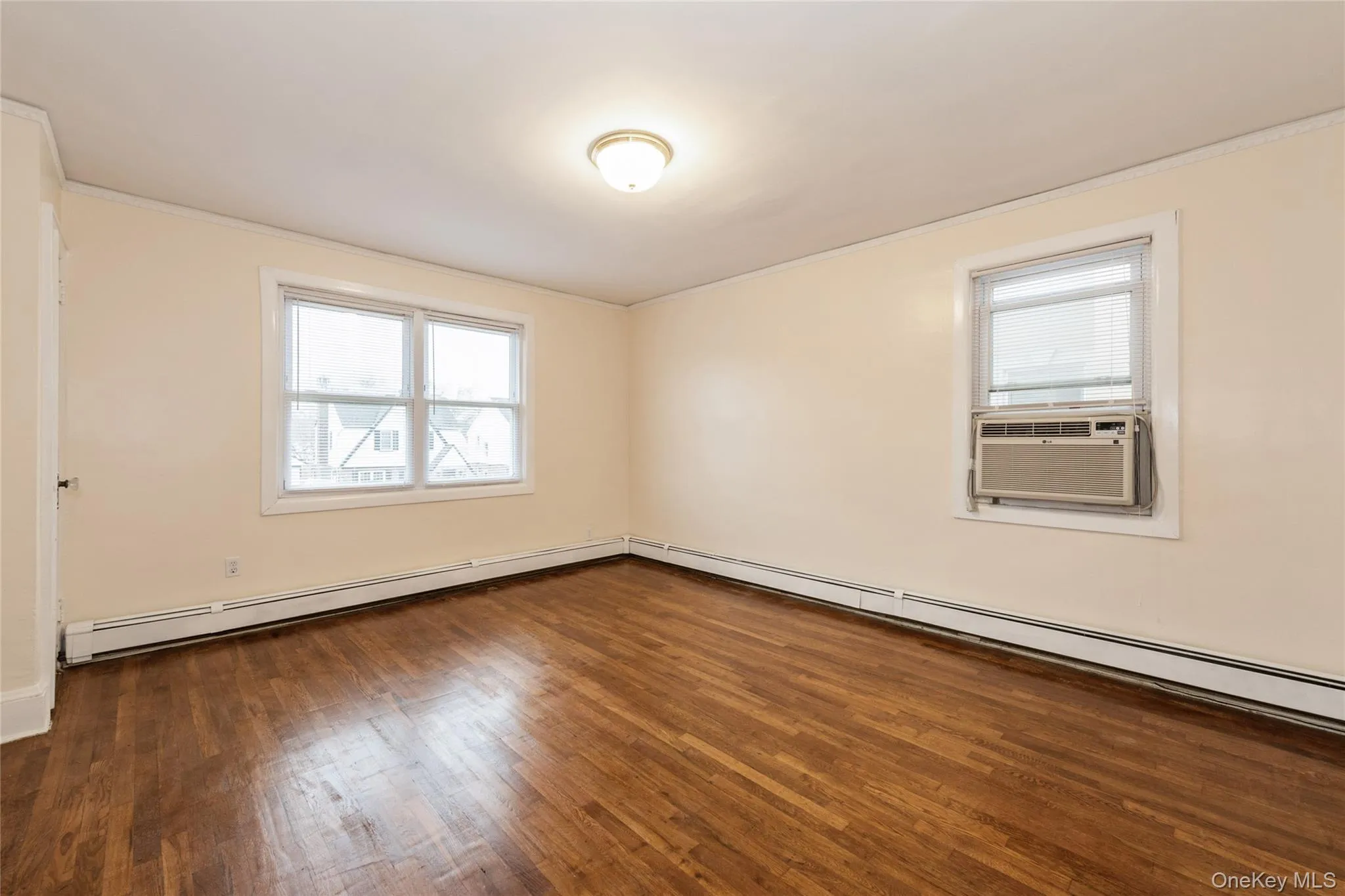 Primary Bedroom featuring hardwood finished floors, baseboard heating, ornamental molding, and A/C unit. Primary Bedroom featuring hardwood finished floors, baseboard heating, ornamental molding, and A/C unit.