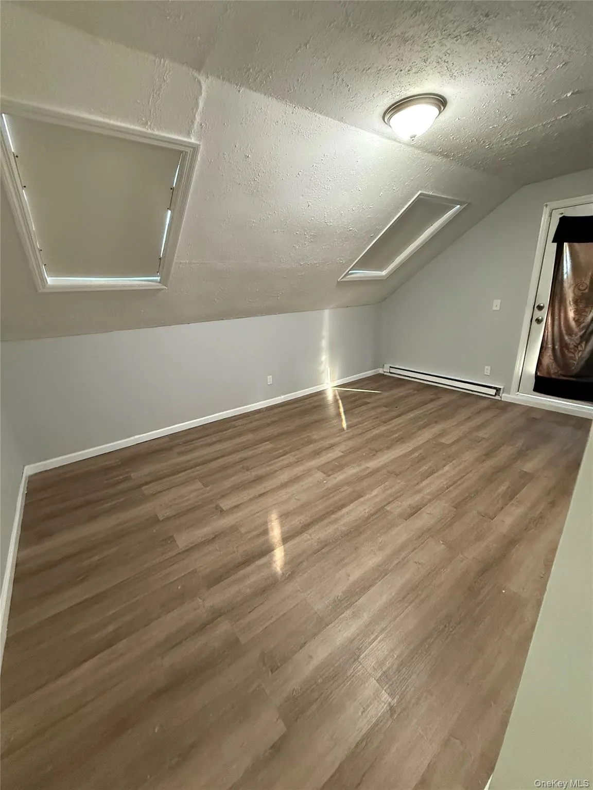 Bonus room featuring a textured ceiling, wood finished floors, lofted ceiling, a baseboard radiator, and attic access Bonus room featuring a textured ceiling, wood finished floors, lofted ceiling, a baseboard radiator, and attic access