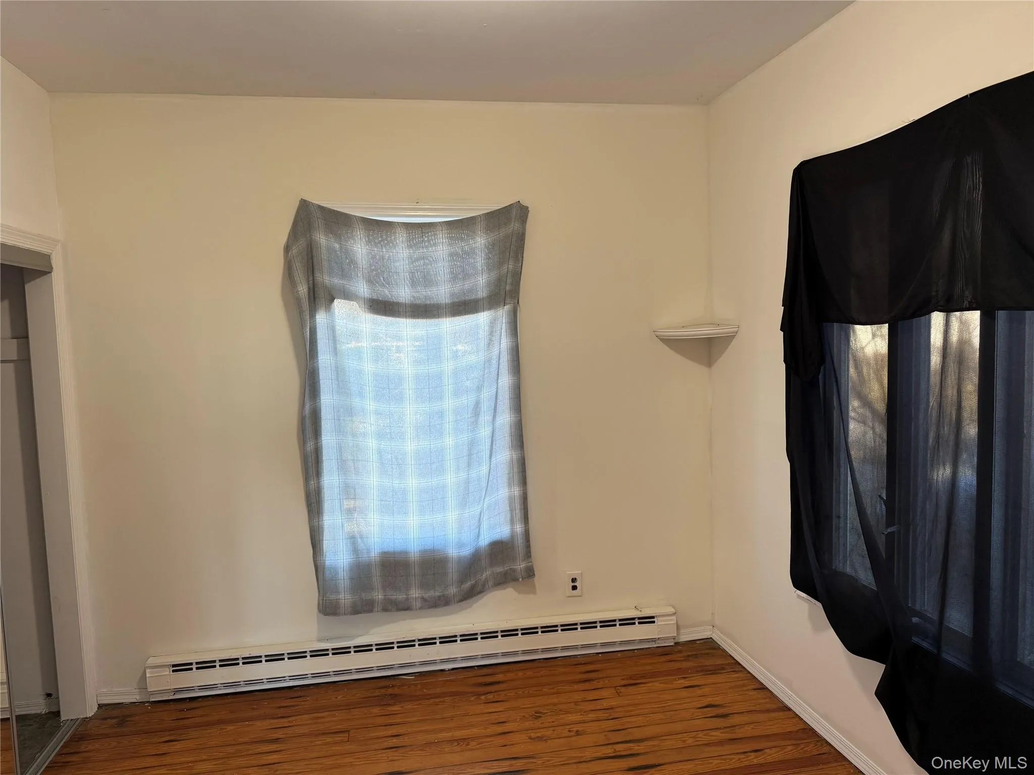 Unfurnished bedroom with baseboard heating and dark wood-style floors Unfurnished bedroom with baseboard heating and dark wood-style floors