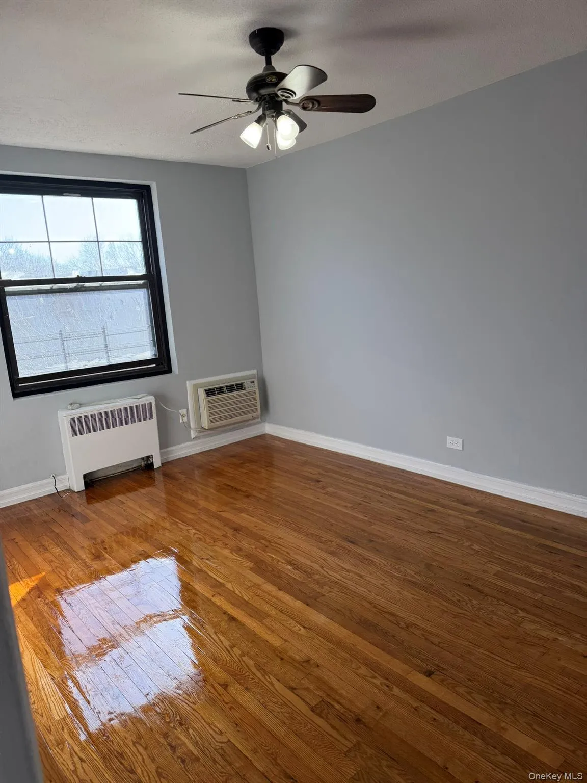 Unfurnished room with wood-type flooring, radiator heating unit, ceiling fan, and a wall mounted AC Unfurnished room with wood-type flooring, radiator heating unit, ceiling fan, and a wall mounted AC