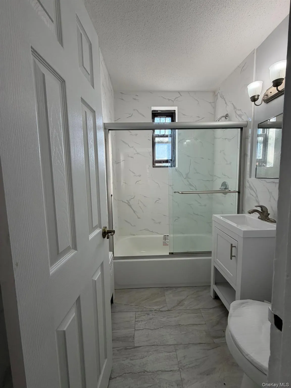Full bathroom with light marble finish floors, bath / shower combo with glass door, vanity, and a textured ceiling Full bathroom with light marble finish floors, bath / shower combo with glass door, vanity, and a textured ceiling