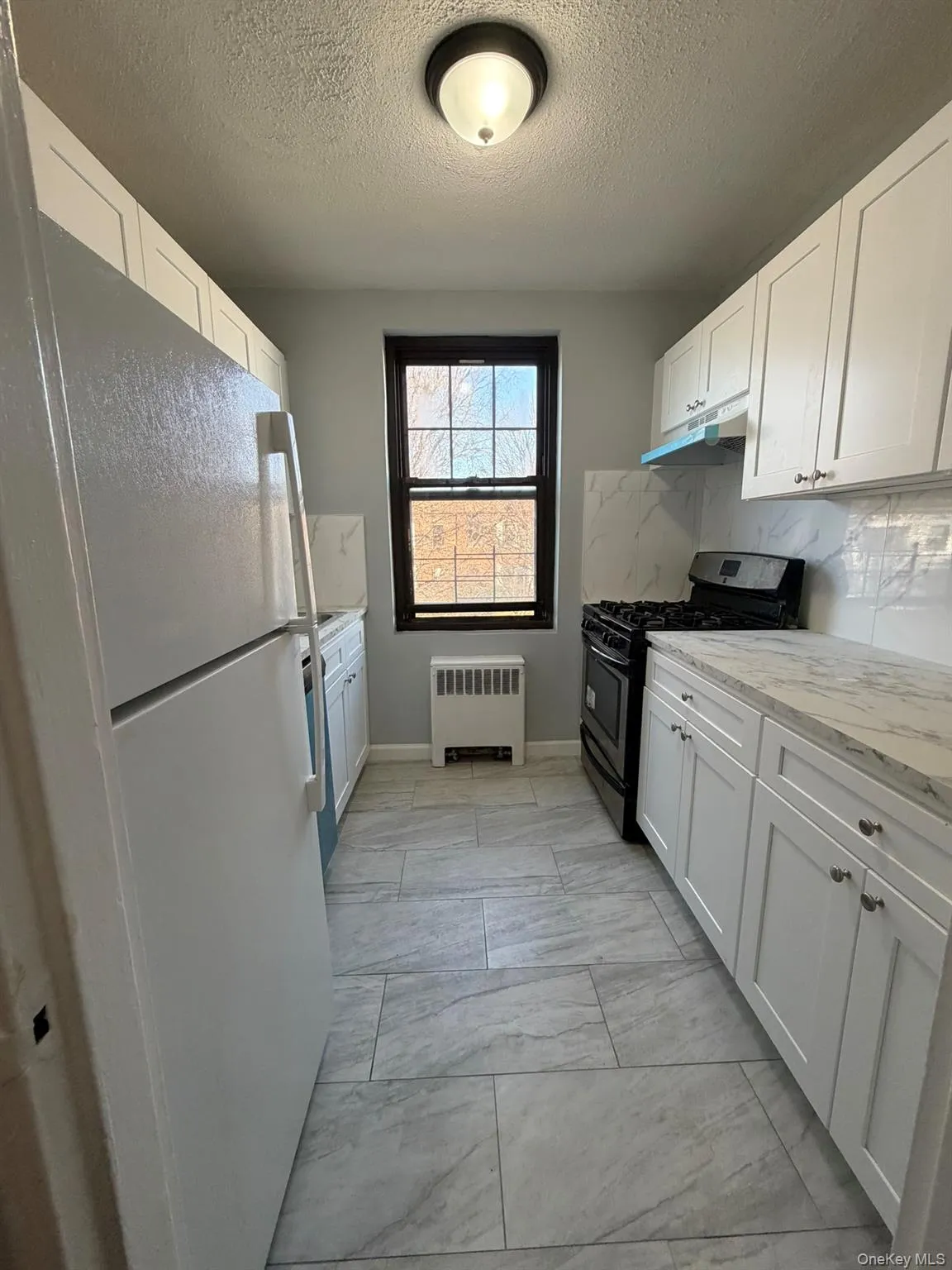 Kitchen featuring gas range oven, white cabinetry, freestanding refrigerator, and a textured ceiling Kitchen featuring gas range oven, white cabinetry, freestanding refrigerator, and a textured ceiling