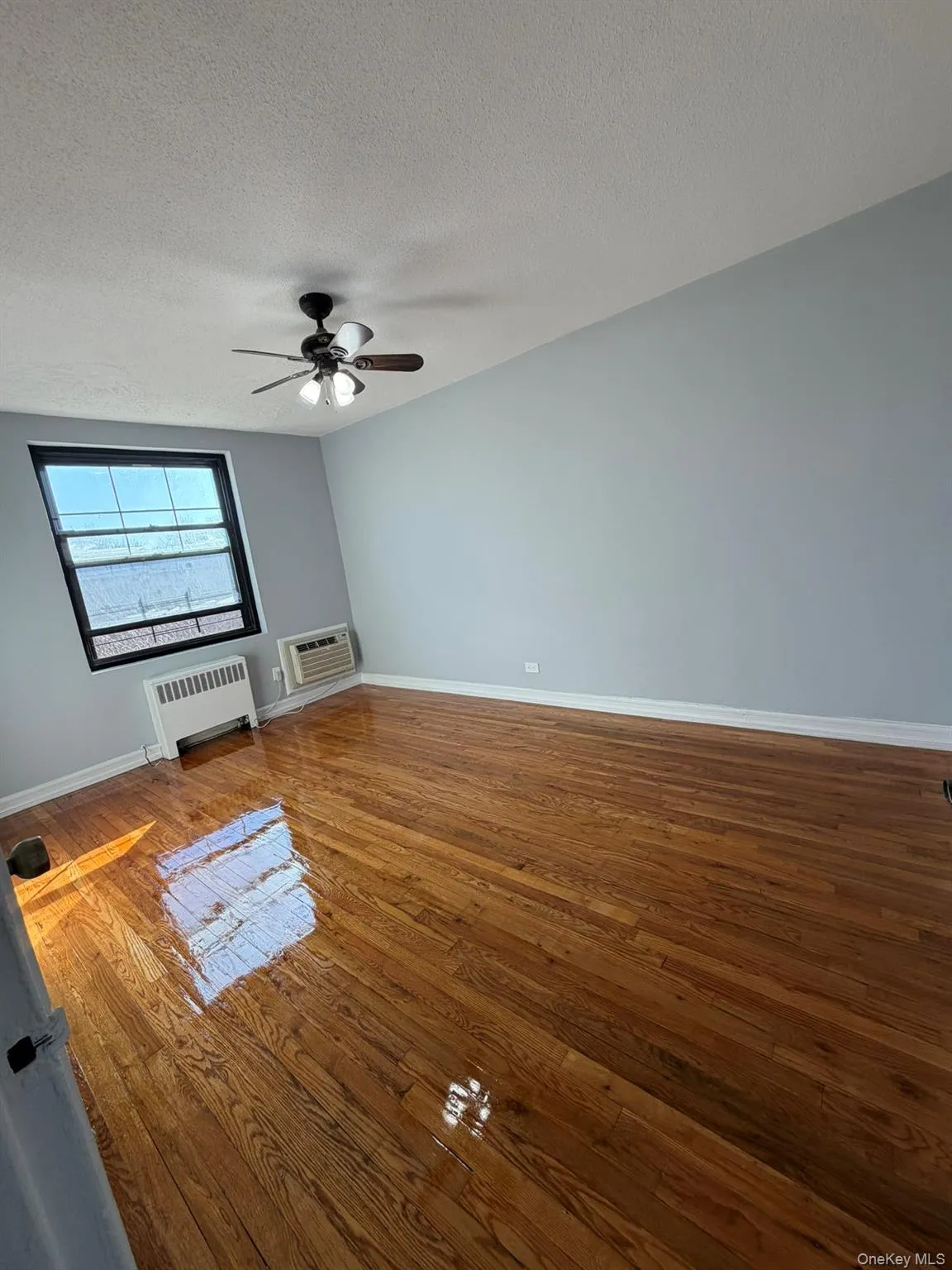 Spare room with radiator heating unit, a textured ceiling, hardwood / wood-style floors, and ceiling fan Spare room with radiator heating unit, a textured ceiling, hardwood / wood-style floors, and ceiling fan
