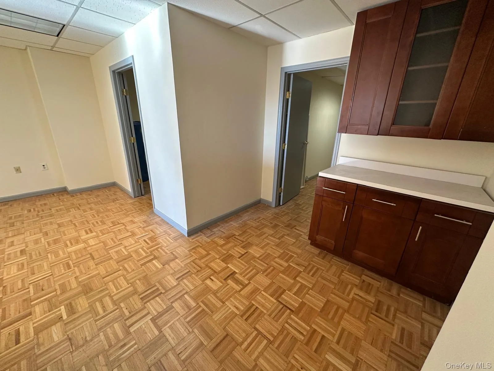 Kitchen featuring a paneled ceiling, light countertops, glass insert cabinets, and dark brown cabinetry Kitchen featuring a paneled ceiling, light countertops, glass insert cabinets, and dark brown cabinetry