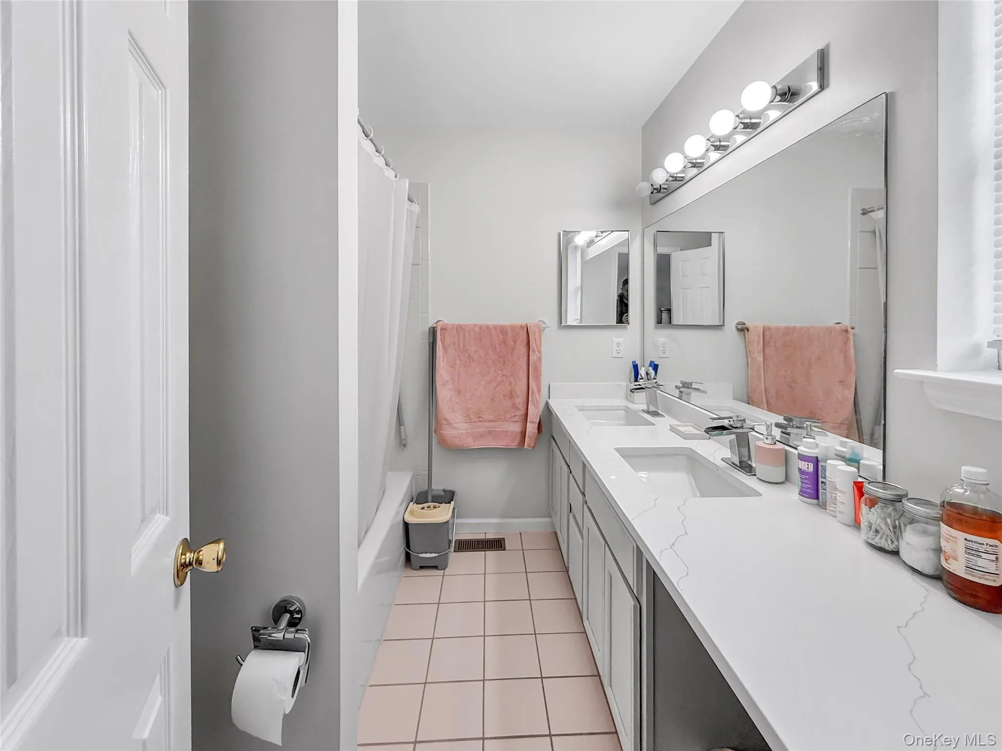 Bathroom featuring double vanity, light tile patterned floors, and shower / bath combo with shower curtain Bathroom featuring double vanity, light tile patterned floors, and shower / bath combo with shower curtain