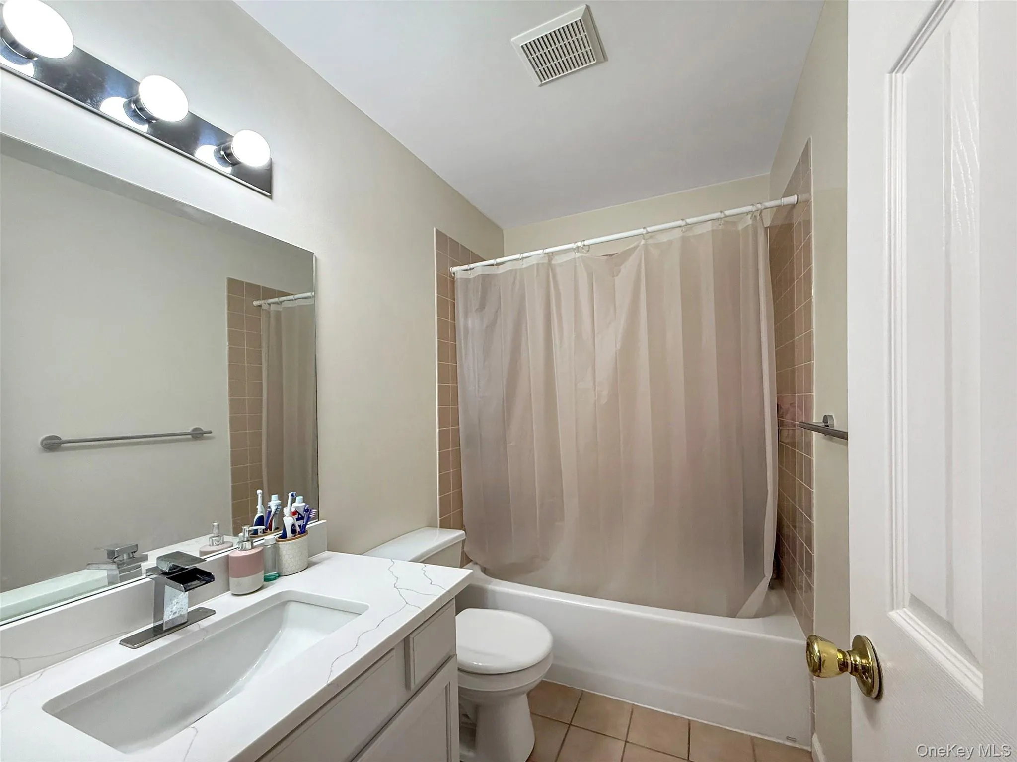 Bathroom featuring vanity, shower / bath combination with curtain, and light tile patterned floors Bathroom featuring vanity, shower / bath combination with curtain, and light tile patterned floors