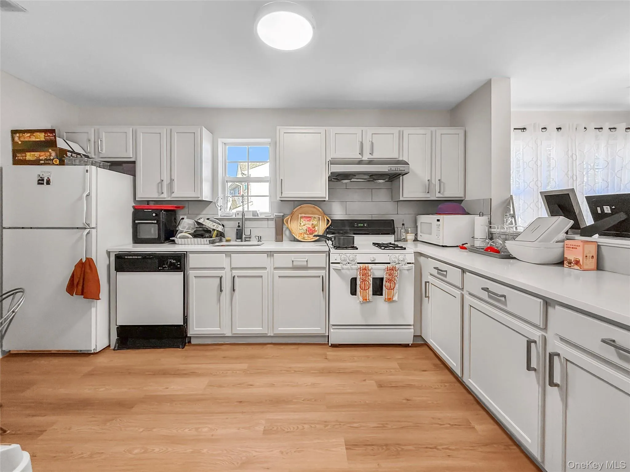 Kitchen featuring white appliances, light countertops, light wood finished floors, under cabinet range hood, and white cabinetry Kitchen featuring white appliances, light countertops, light wood finished floors, under cabinet range hood, and white cabinetry