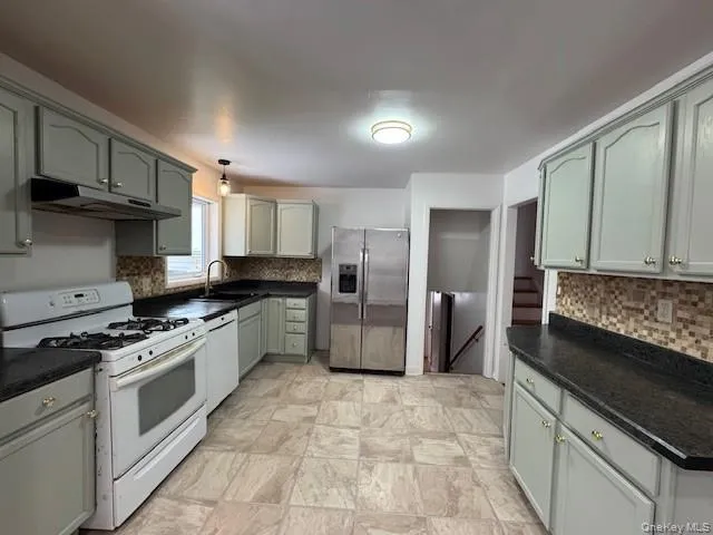 Kitchen with white appliances, tasteful backsplash, under cabinet range hood, and pendant lighting Kitchen with white appliances, tasteful backsplash, under cabinet range hood, and pendant lighting