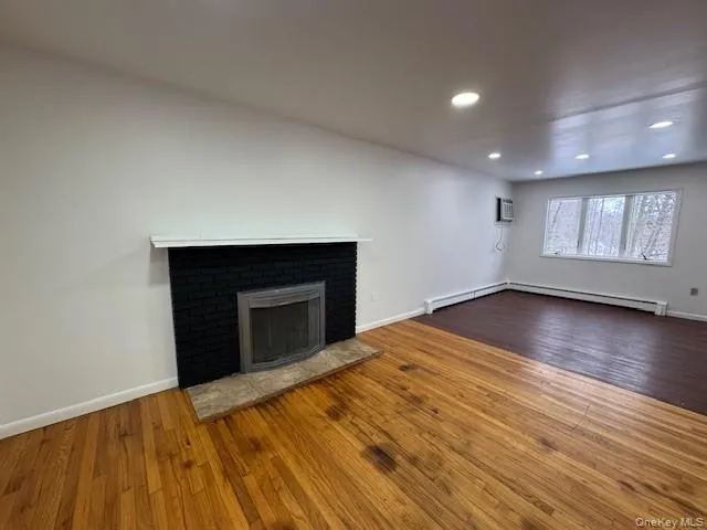 Unfurnished living room featuring dark wood-style flooring, a fireplace, recessed lighting, and baseboard heating Unfurnished living room featuring dark wood-style flooring, a fireplace, recessed lighting, and baseboard heating
