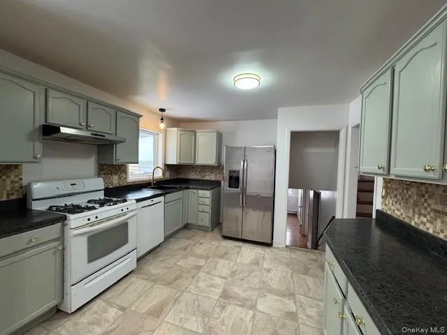 Kitchen featuring dark countertops, tasteful backsplash, white appliances, and under cabinet range hood Kitchen featuring dark countertops, tasteful backsplash, white appliances, and under cabinet range hood