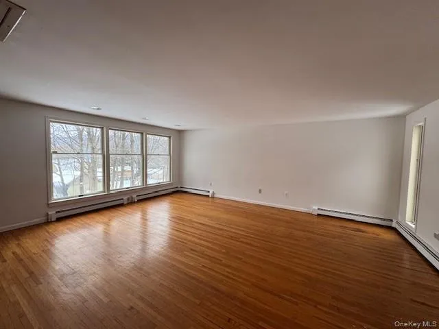 Empty room with hardwood / wood-style floors and a baseboard radiator Empty room with hardwood / wood-style floors and a baseboard radiator