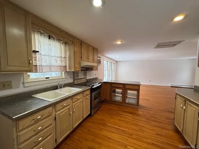 Kitchen featuring a peninsula, dark wood-style floors, stainless steel range with electric cooktop, dark countertops, and open floor plan Kitchen featuring a peninsula, dark wood-style floors, stainless steel range with electric cooktop, dark countertops, and open floor plan