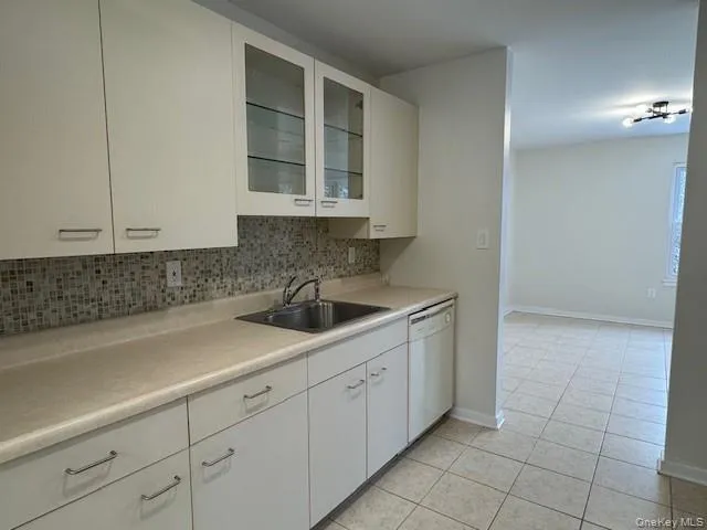 Kitchen with white cabinets, light countertops, glass insert cabinets, backsplash, and light tile patterned flooring Kitchen with white cabinets, light countertops, glass insert cabinets, backsplash, and light tile patterned flooring