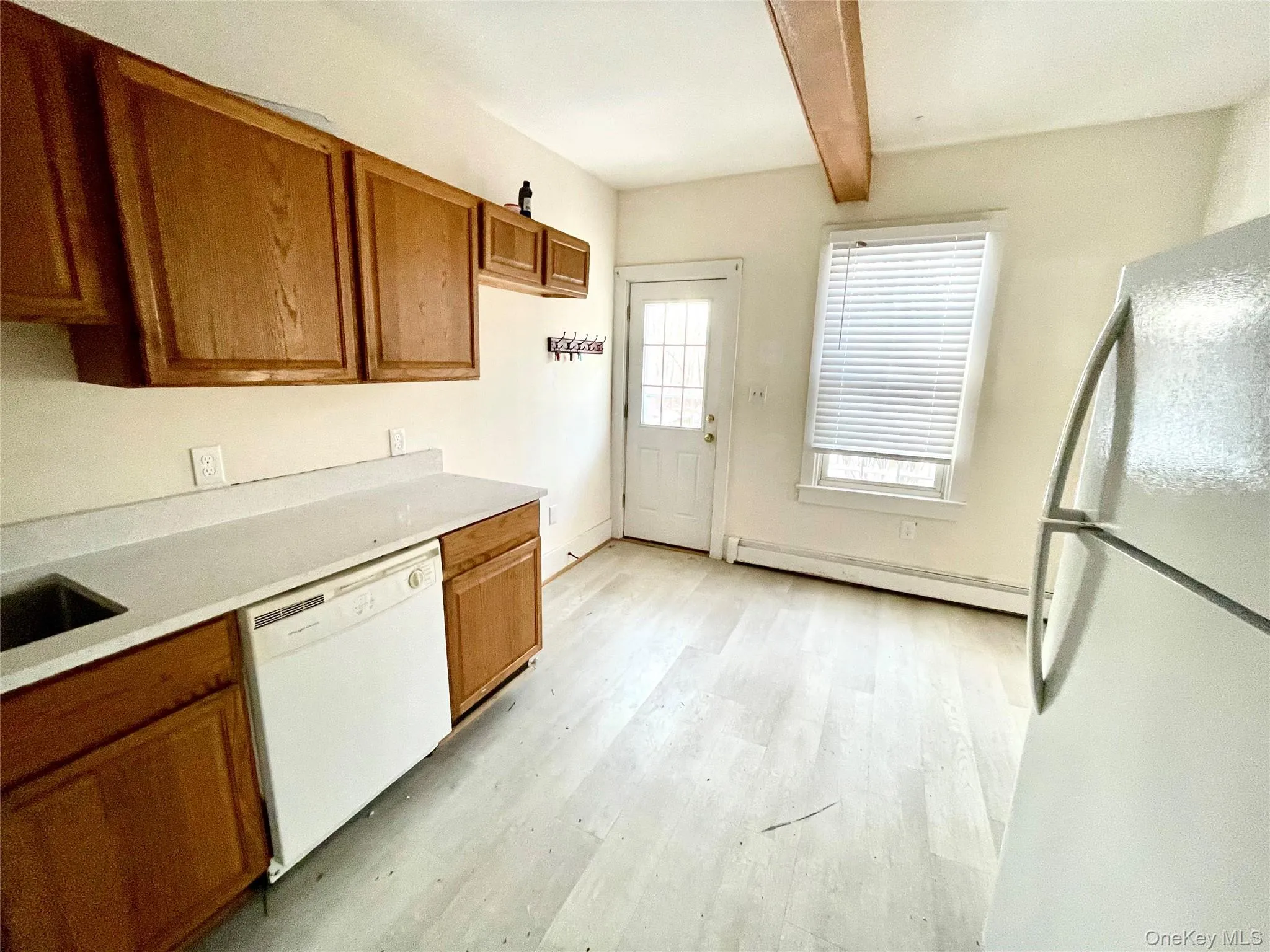 Kitchen featuring white appliances, brown cabinets, a baseboard heating unit, beam ceiling, and light wood finished floors Kitchen featuring white appliances, brown cabinets, a baseboard heating unit, beam ceiling, and light wood finished floors